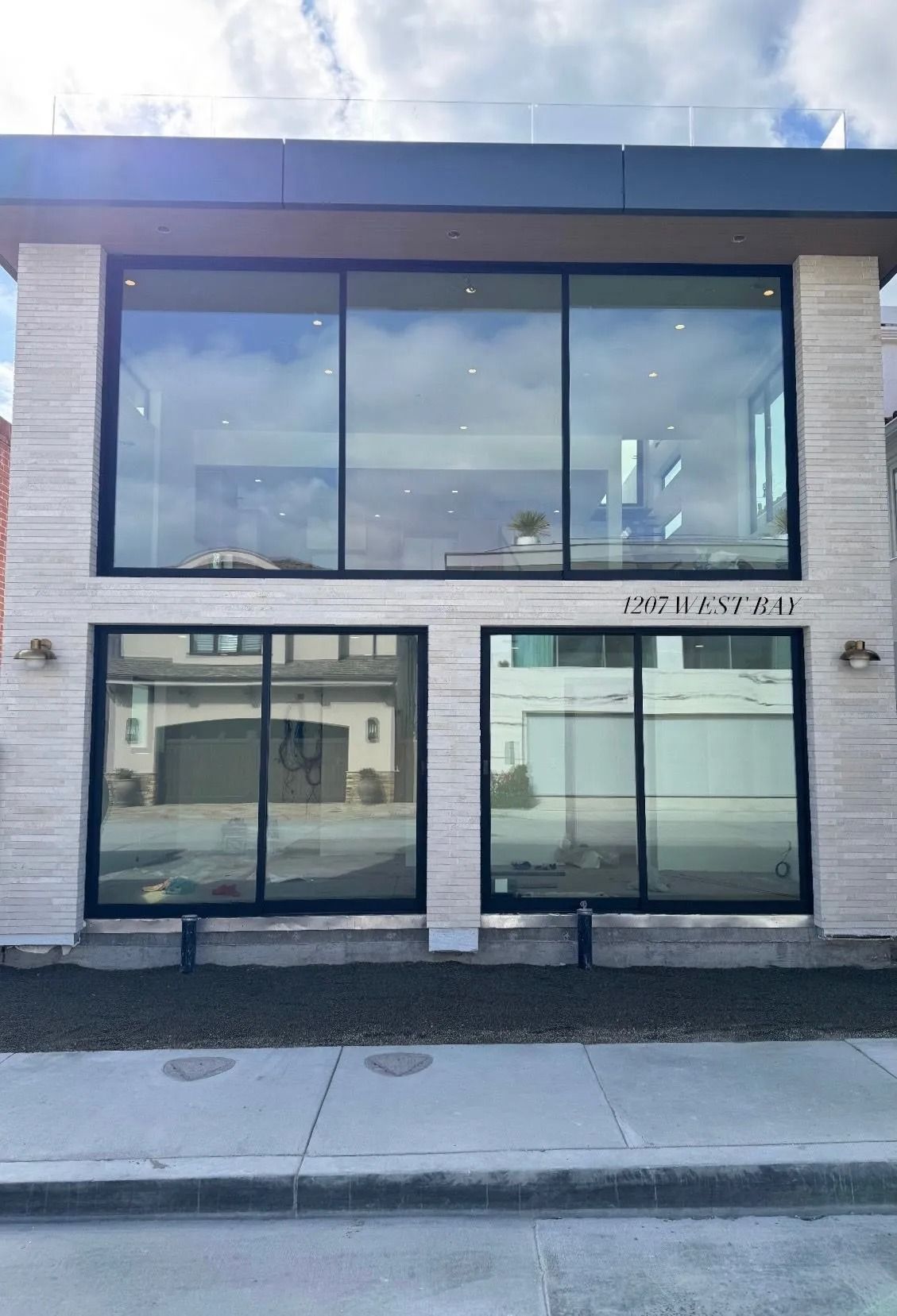 Modern two-story building with large glass windows and black frames. Exterior has light-colored stone accents. Street number 