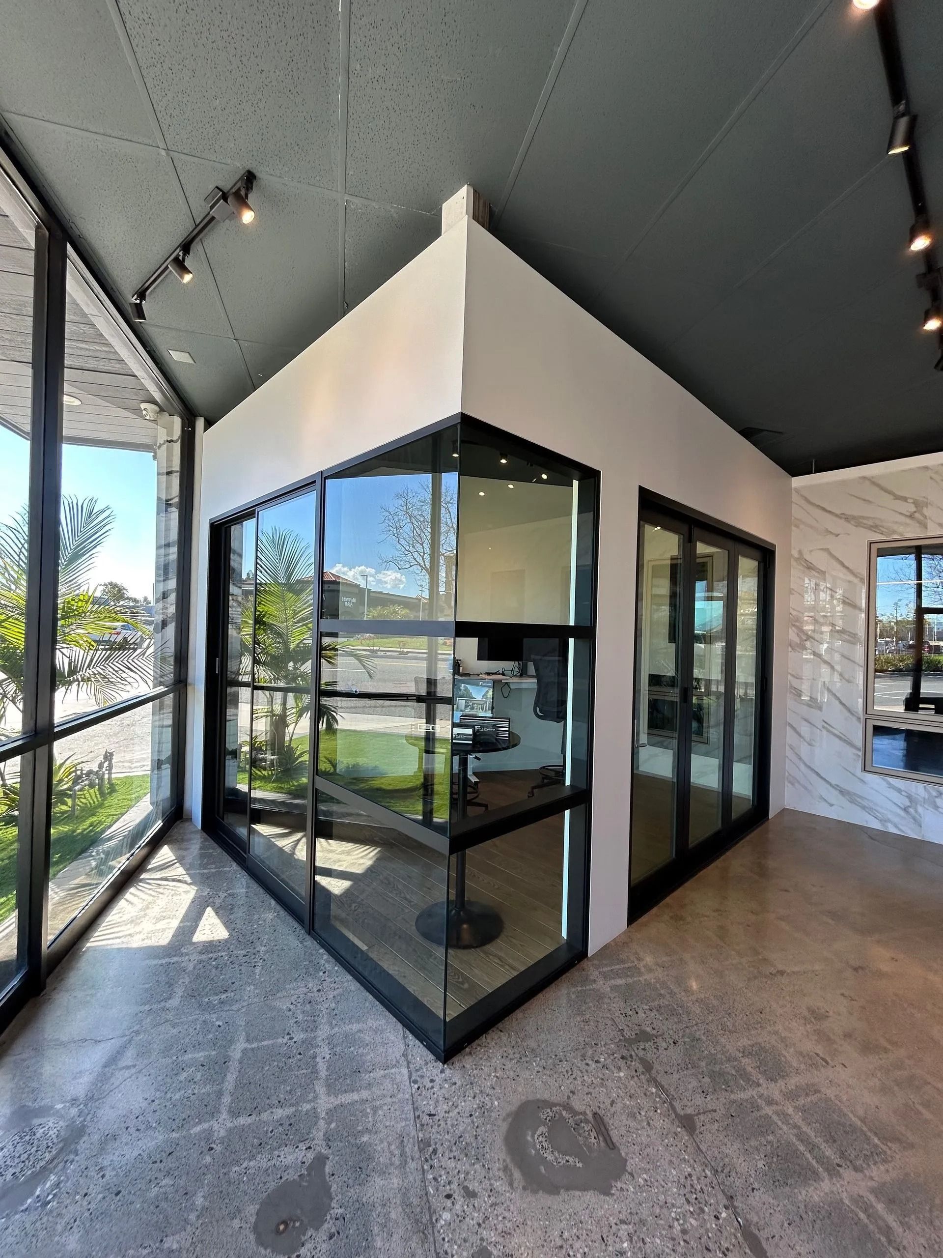 Modern office space with glass walls and black frames. Sunlight streams in.