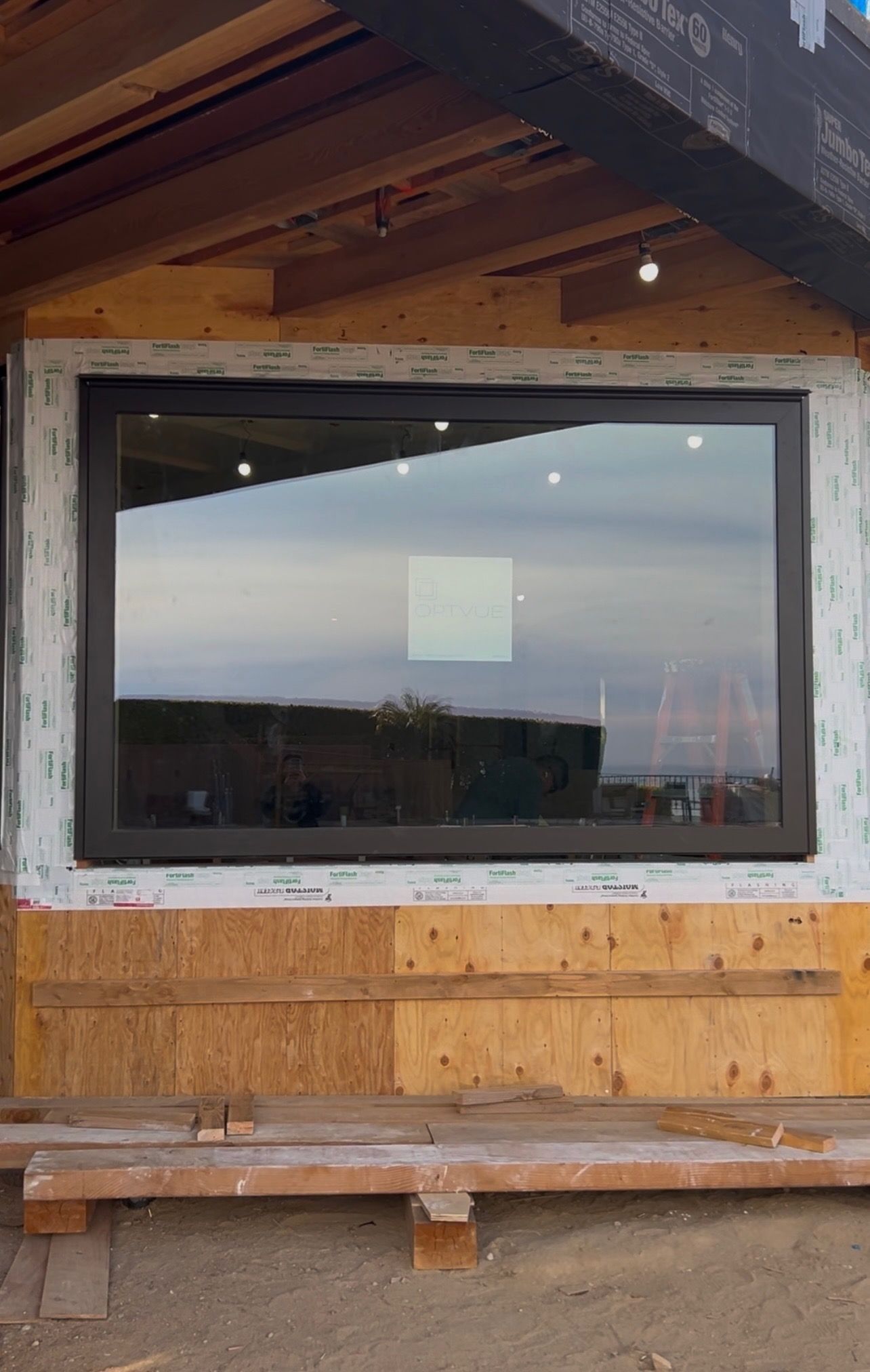 Large rectangular window installed on a building under construction; reflective glass, dark brown frame.