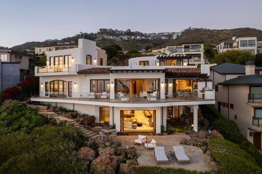 White villa overlooking the ocean, with open terraces and lounge chairs.