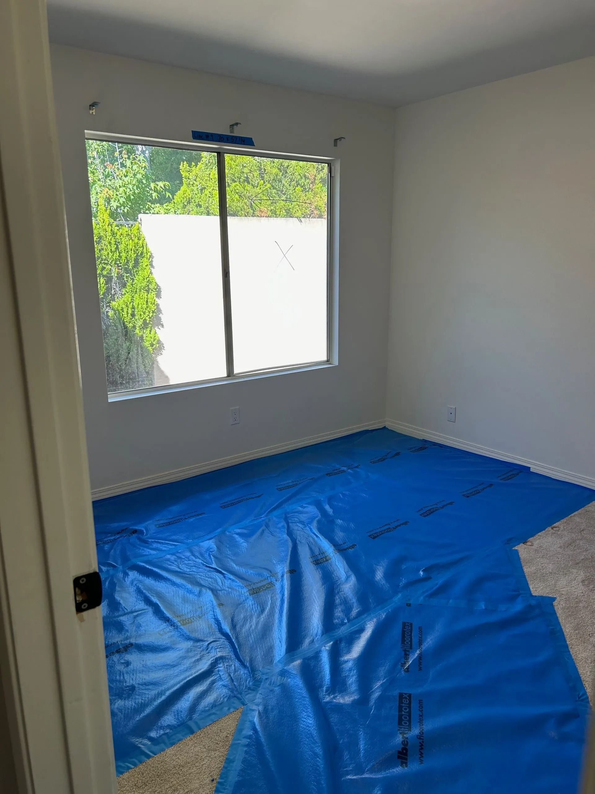 Room with white walls and a window. Blue tarp covers the floor.