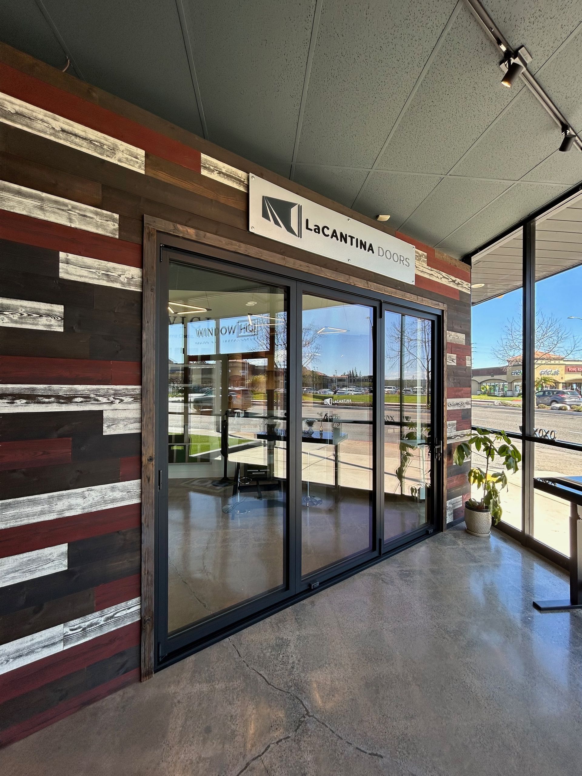 Exterior of business with glass doors, and sign, surrounded by brick and wood siding.