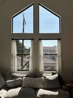 Living room with tall windows, sheer curtains, and a couch. Outside, a utility pole is visible.