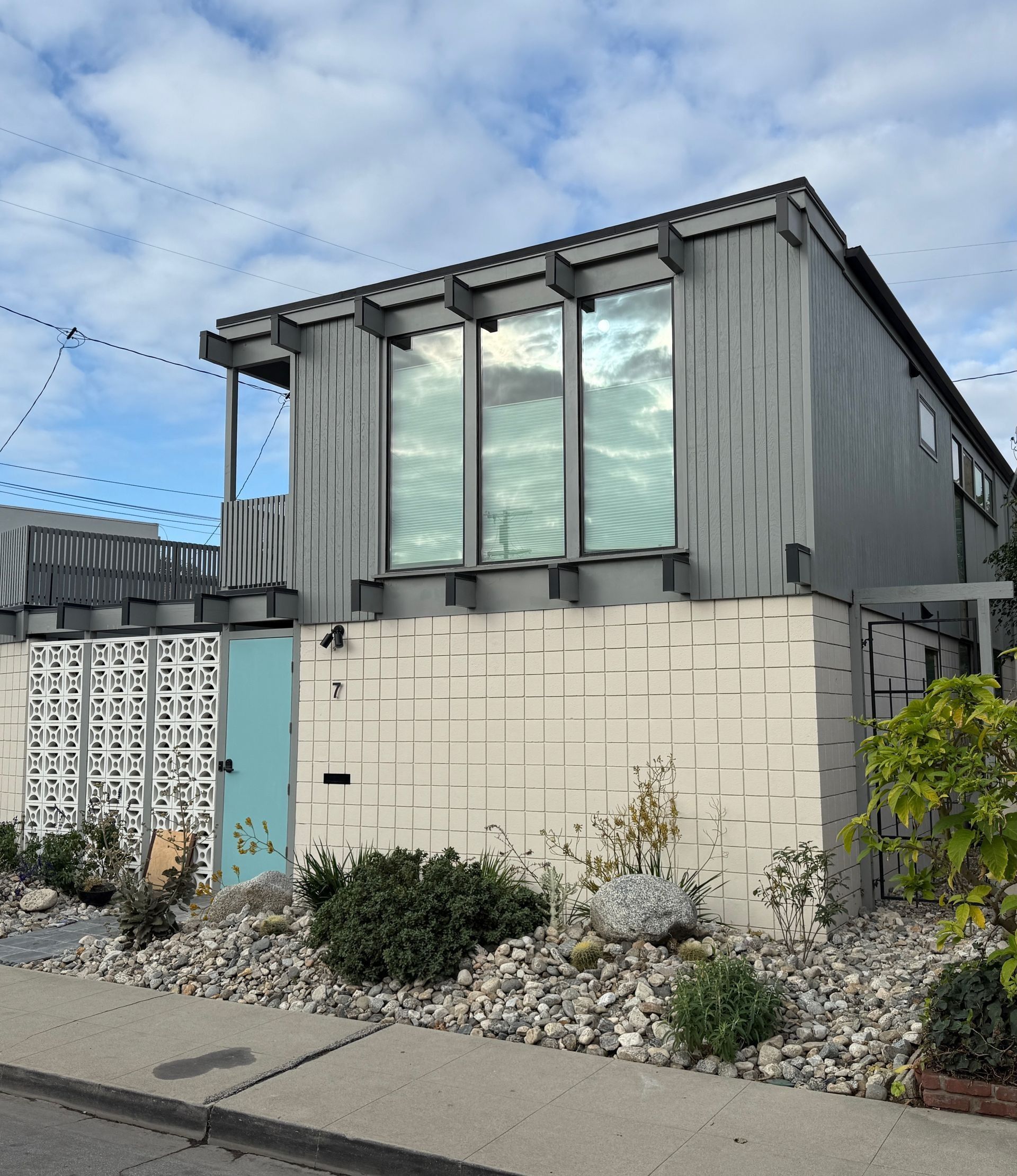 Gray two-story house with large windows, light blue door, and textured white wall. Rocky landscaping in front.