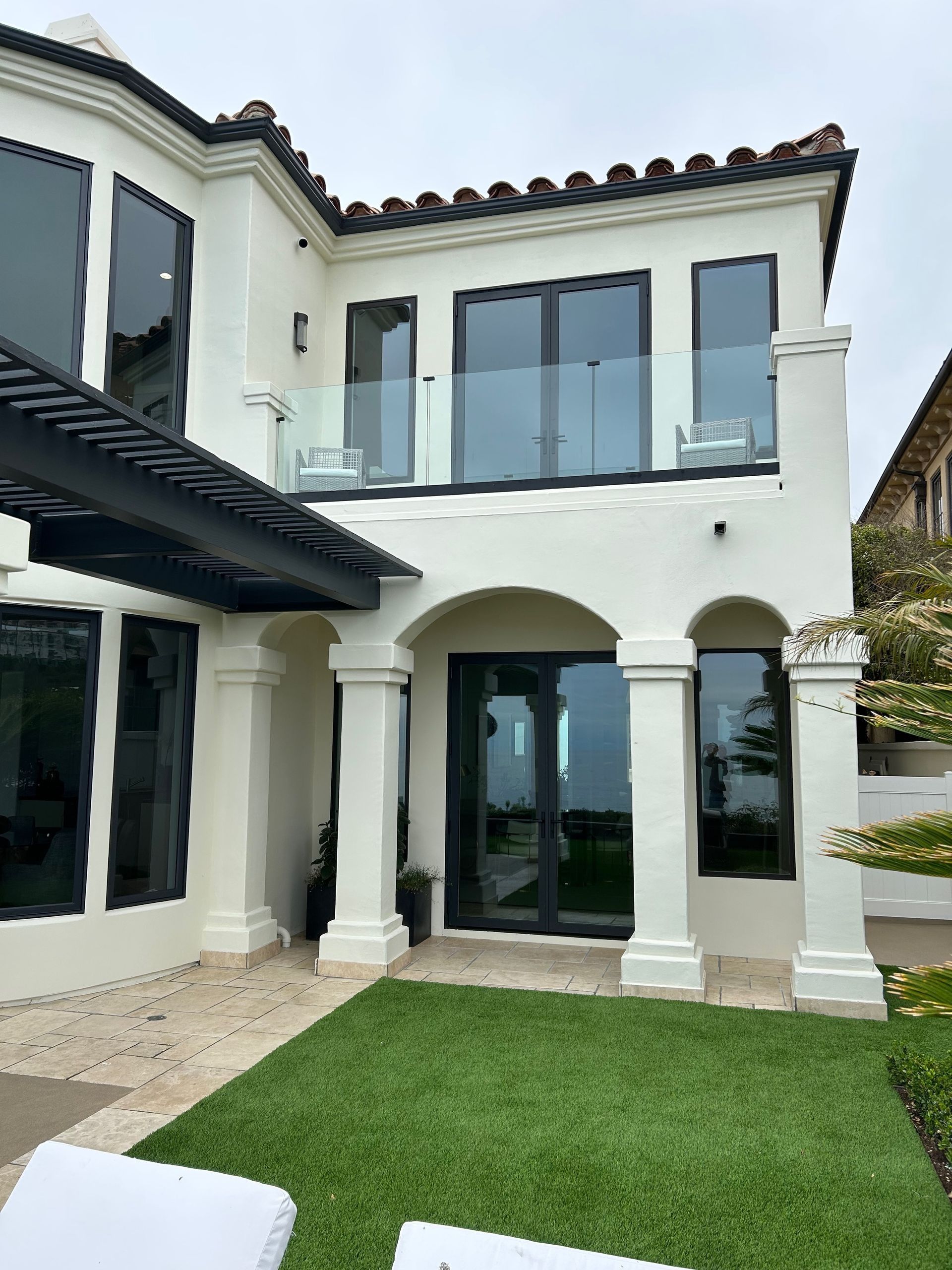 White stucco luxury home with black-framed windows and a small balcony. Artificial turf lawn.