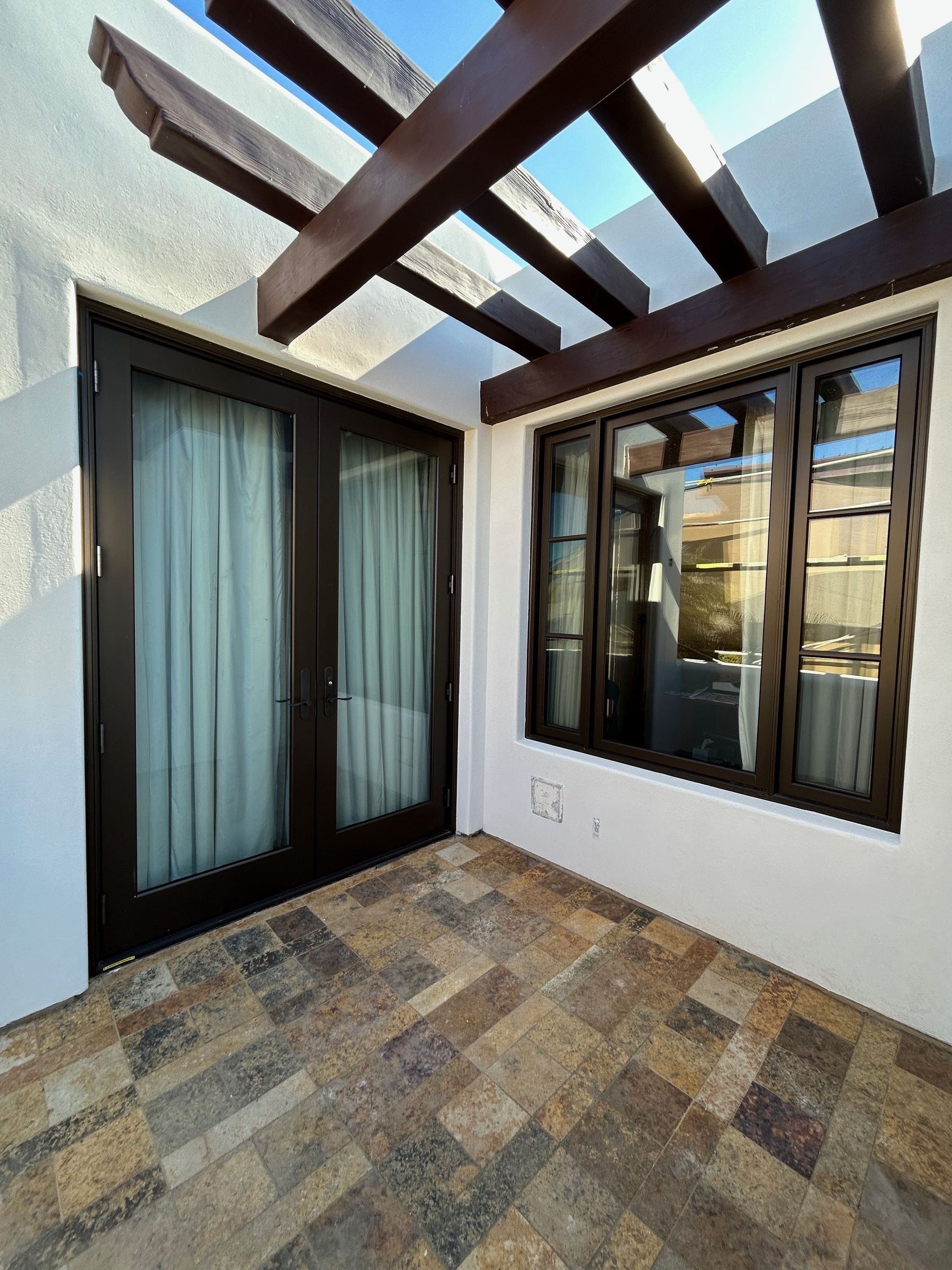 Patio with dark wood doors, windows, and pergola against white walls, stone floor.