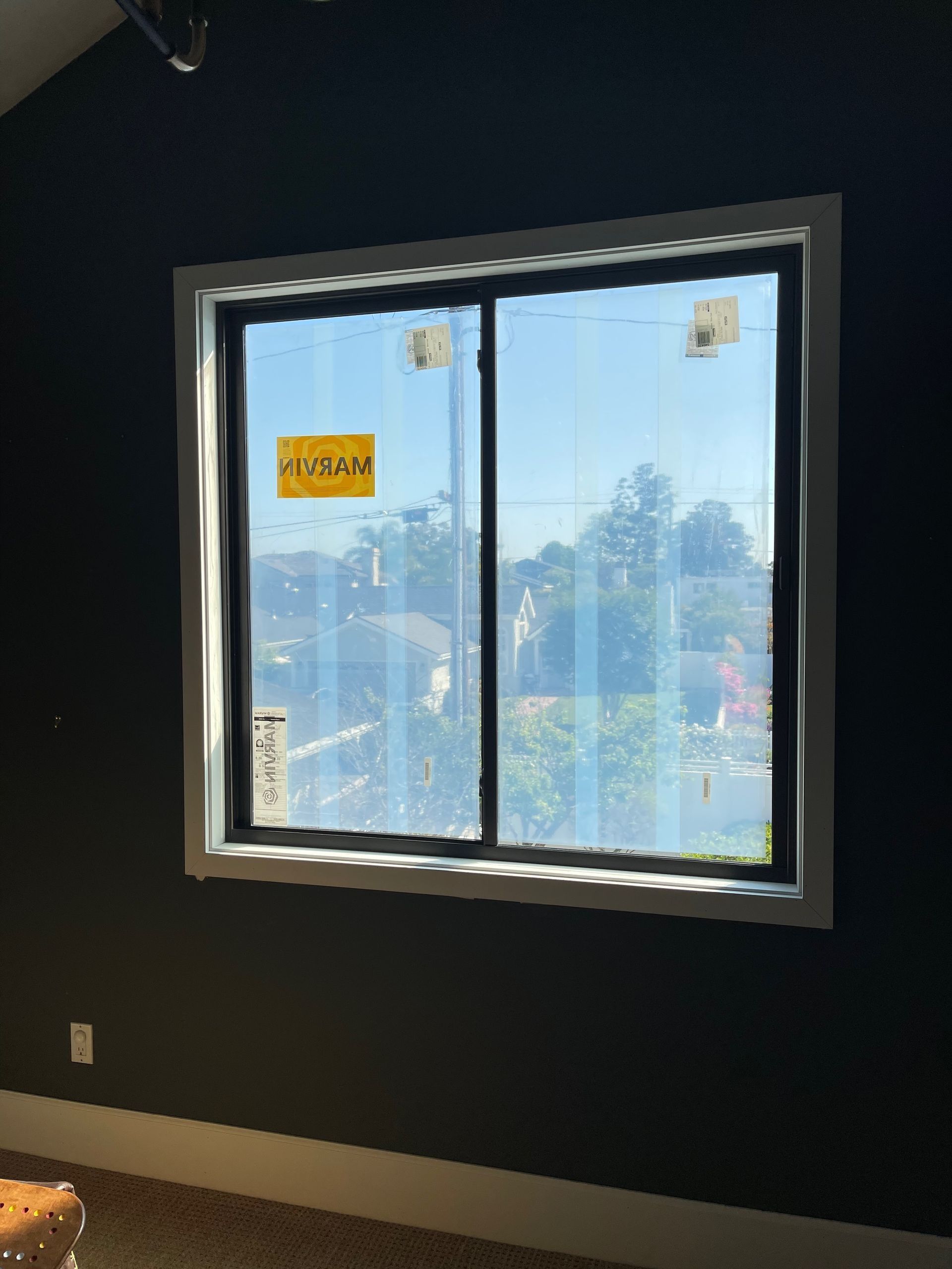 Window in a room with dark walls and white trim. Window covered in protective film, outside view.