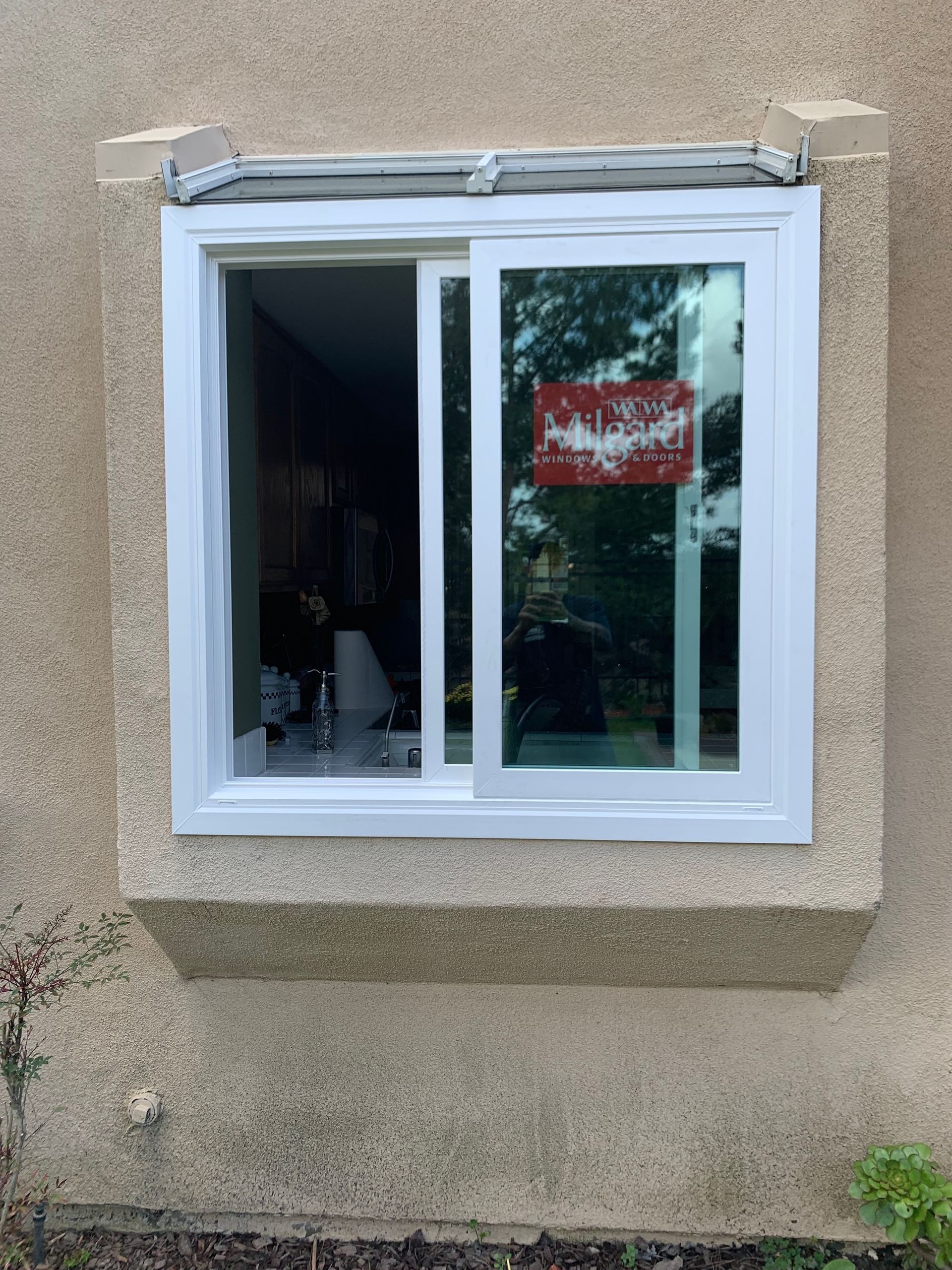 White sliding window in a beige stucco wall; a red sign is visible inside the window's glass.