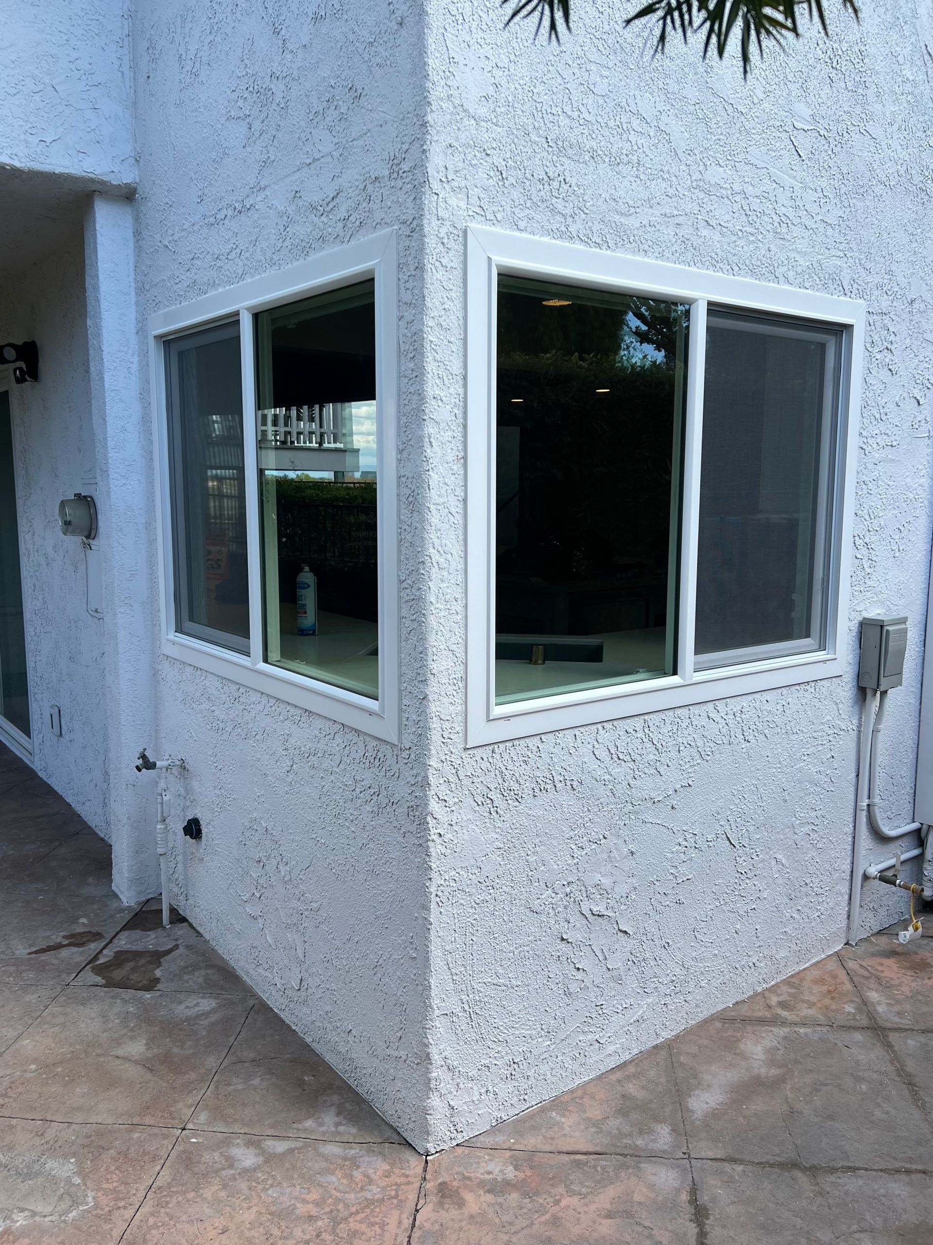 Exterior corner of a building with white-framed windows, stucco walls, and a tiled patio.