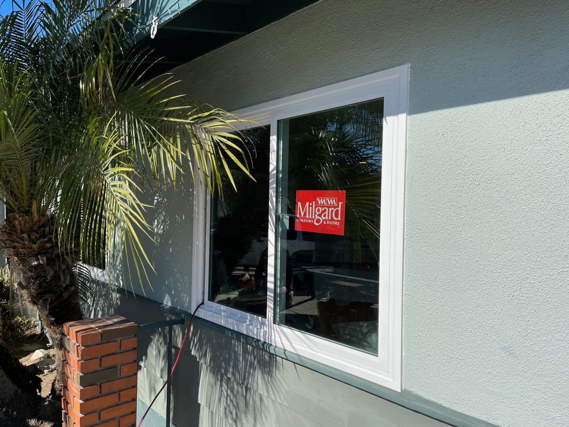 A white-framed sliding window on a light blue stucco exterior. A red sign is visible inside the window.
