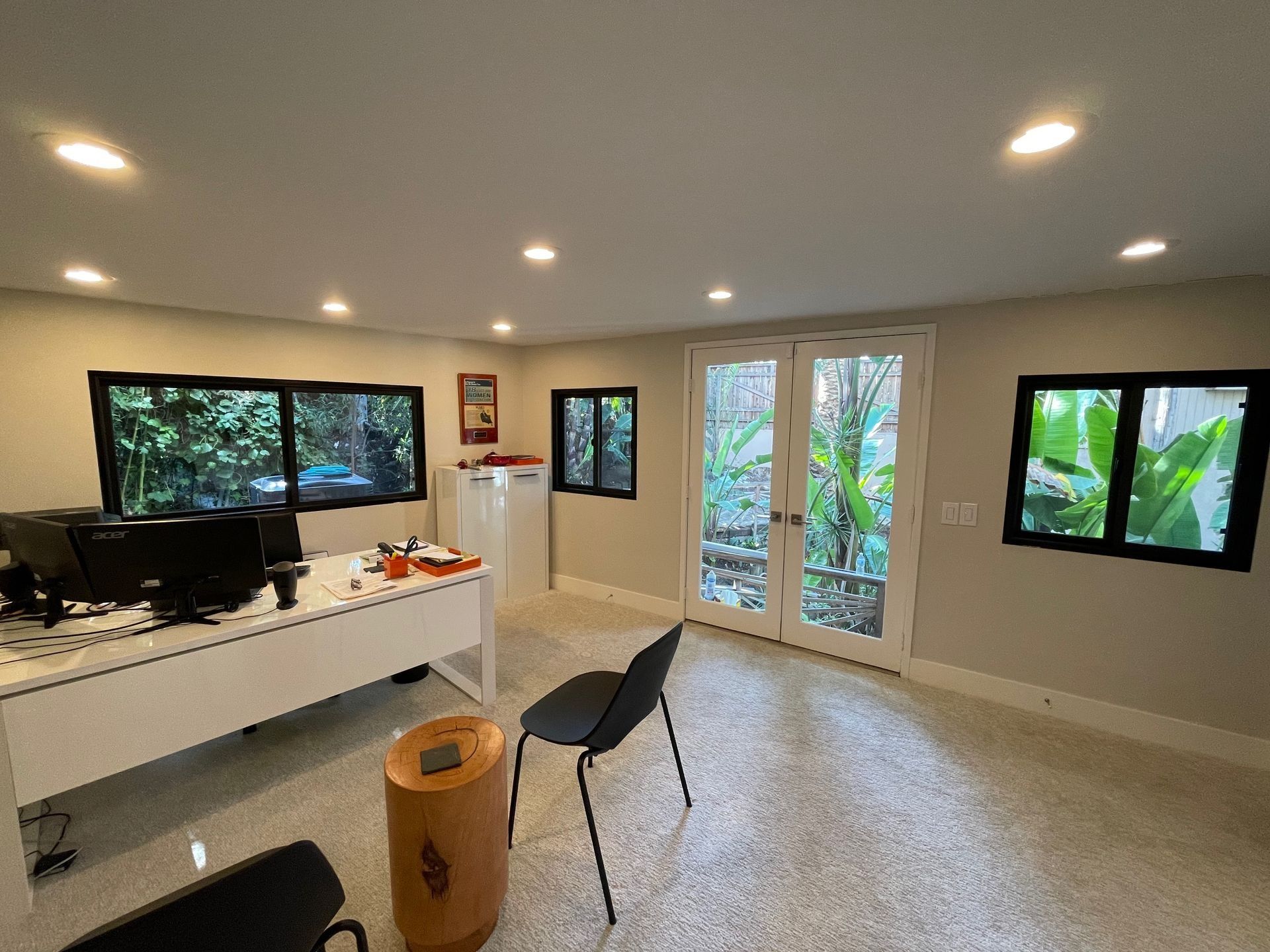 Office with desk, windows, and glass doors looking out onto greenery. Light-colored walls and flooring.