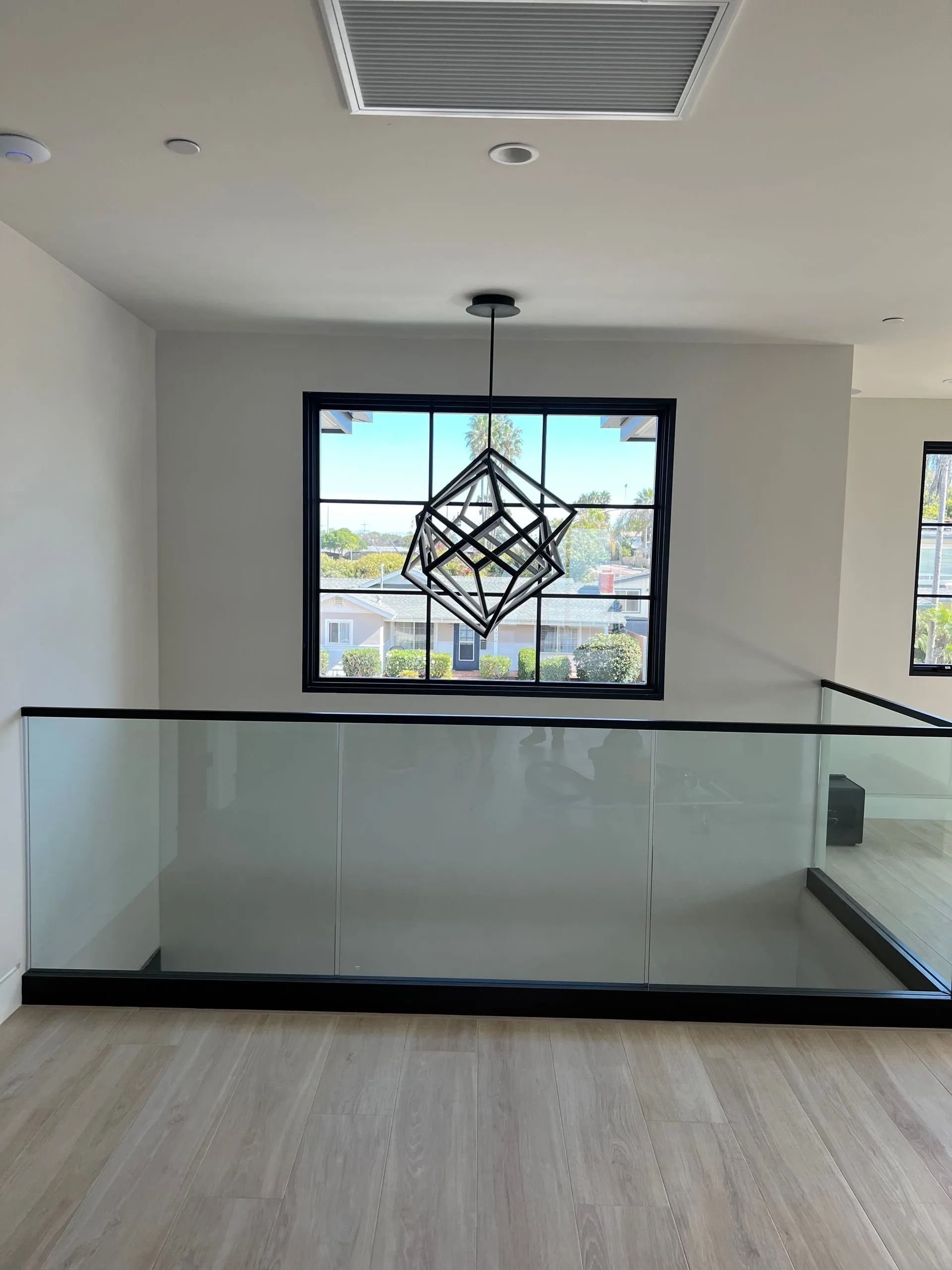 Interior view: modern loft with glass railing, large window, and geometric chandelier.