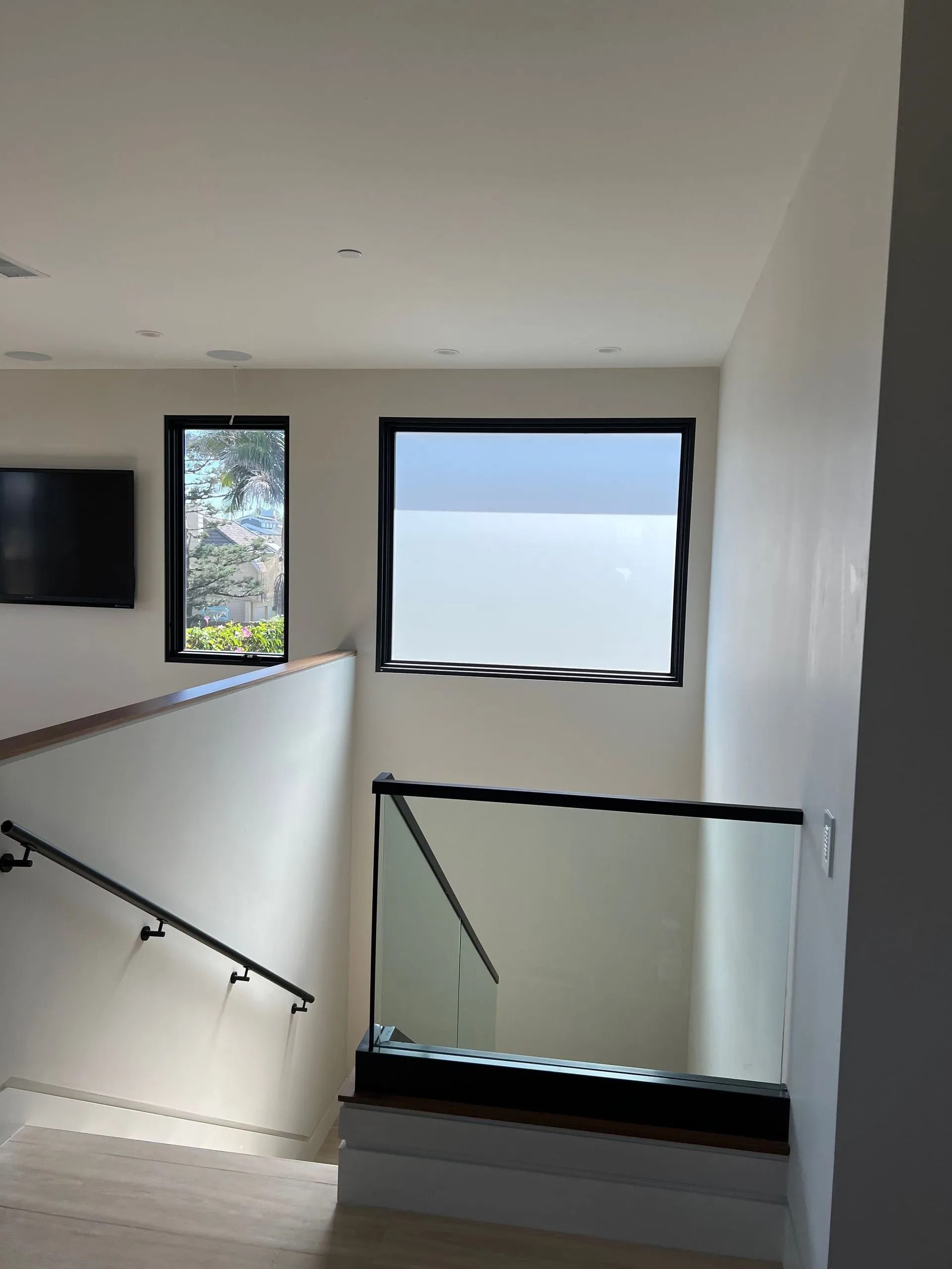 Interior view of a staircase with glass railings and black-framed windows; natural light.