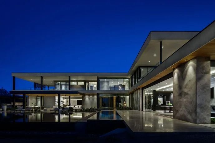 Modern luxury home exterior at dusk, with large windows, open floor plan, and illuminated pool.