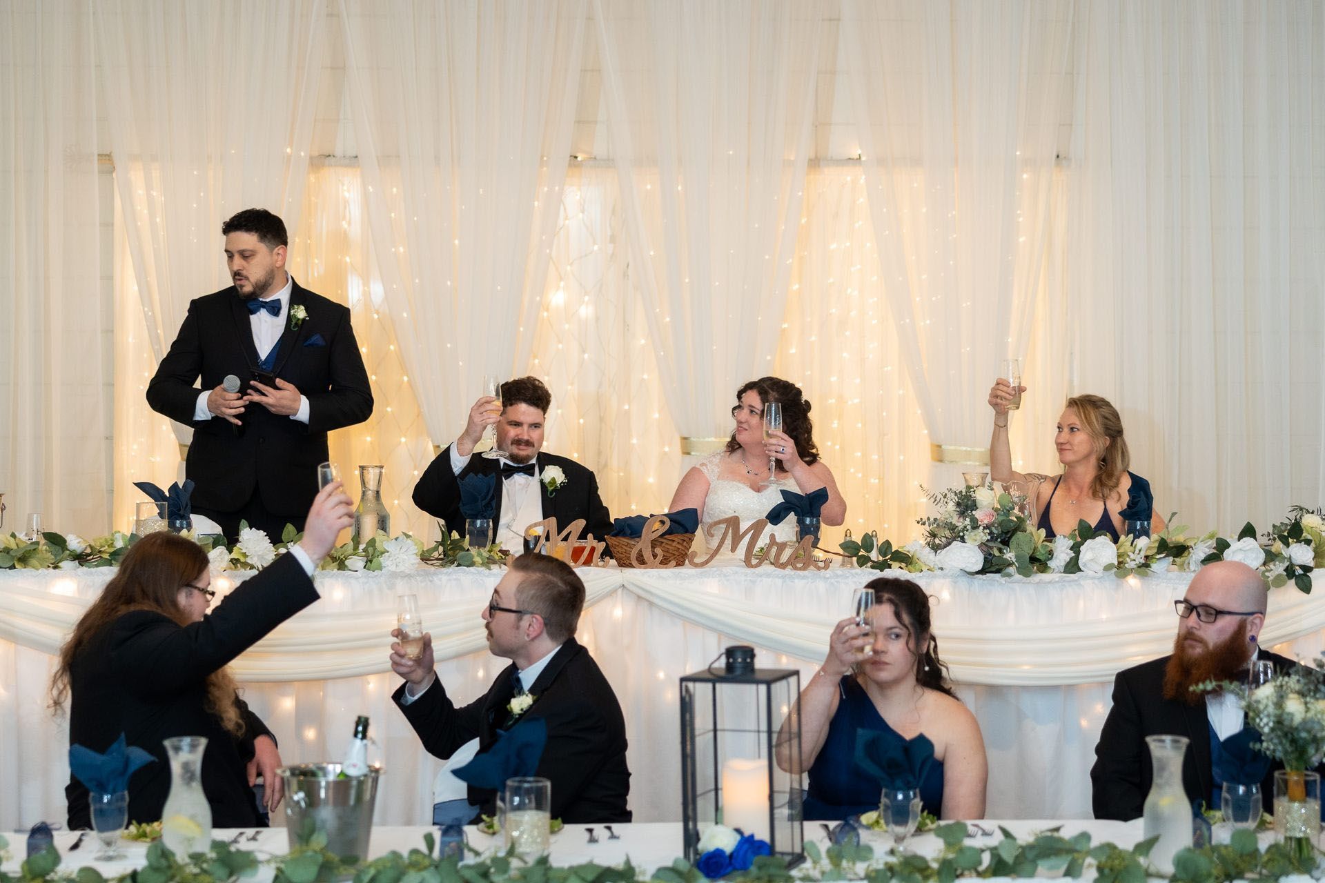Wedding reception toast at a decorated head table with the bridal party seated behind it