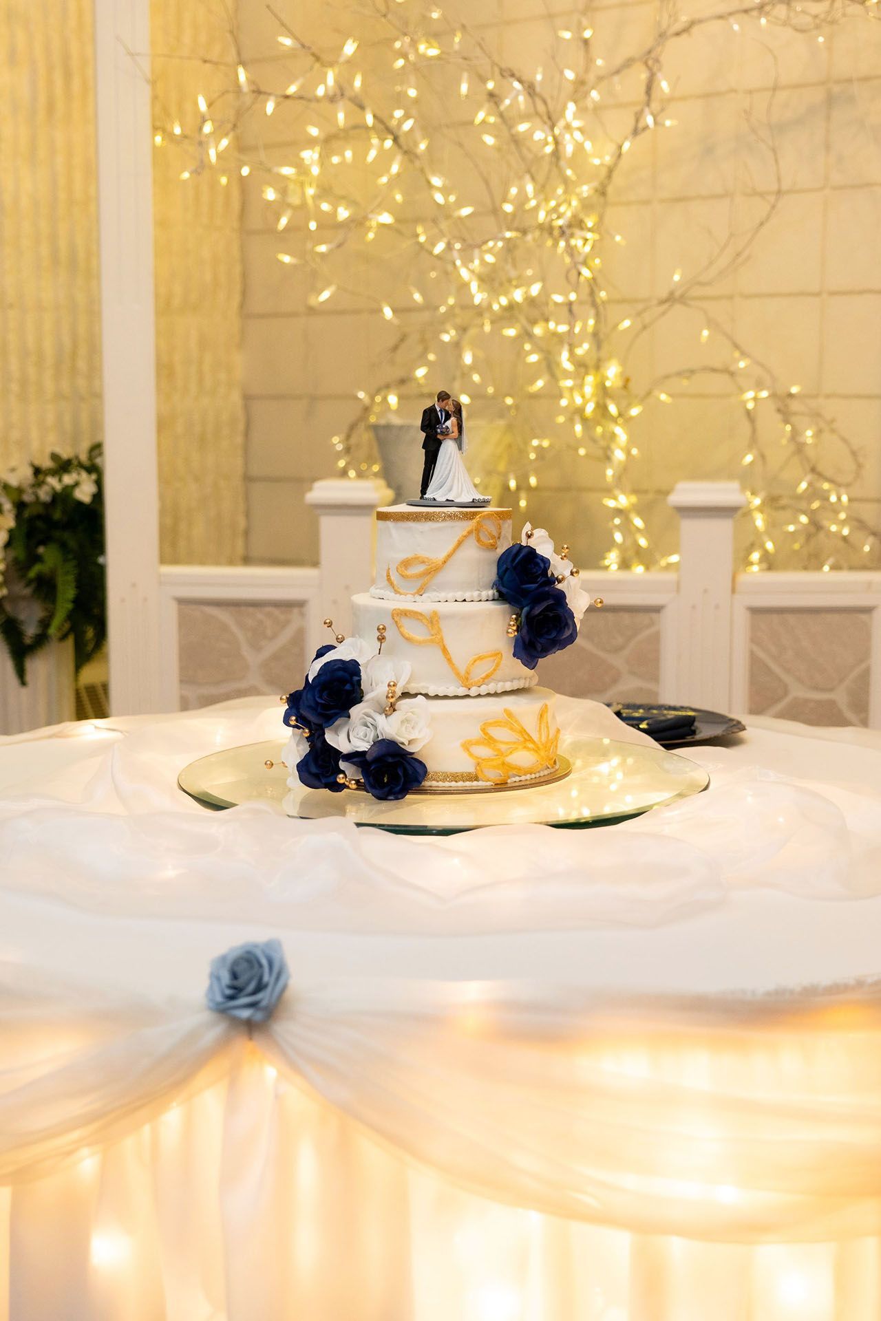 Tiered white cake with blue flowers on a lit dessert table at a wedding reception