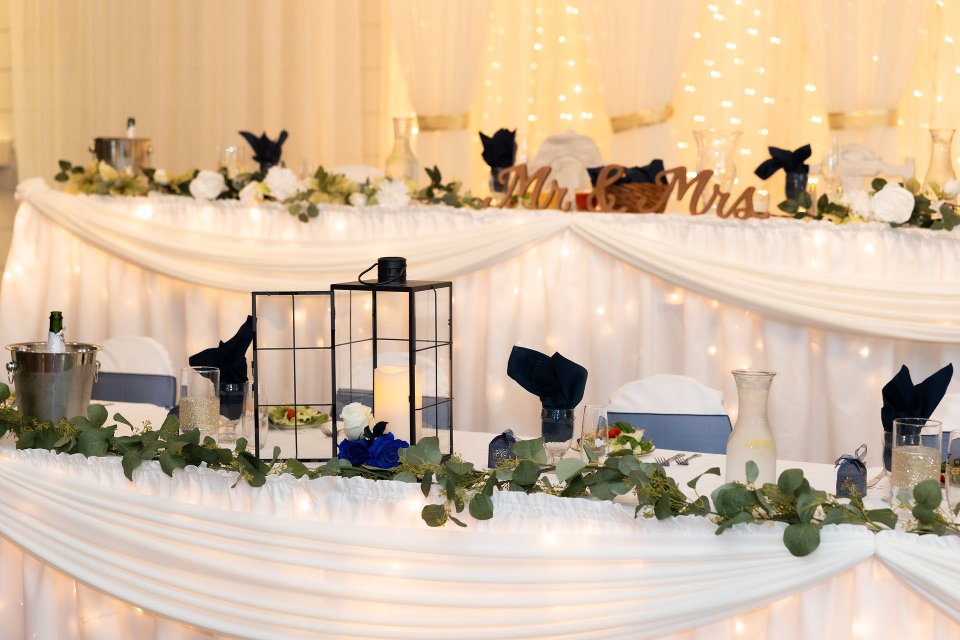 Elegant draped banquet table with candles, greenery, and lanterns at a celebration