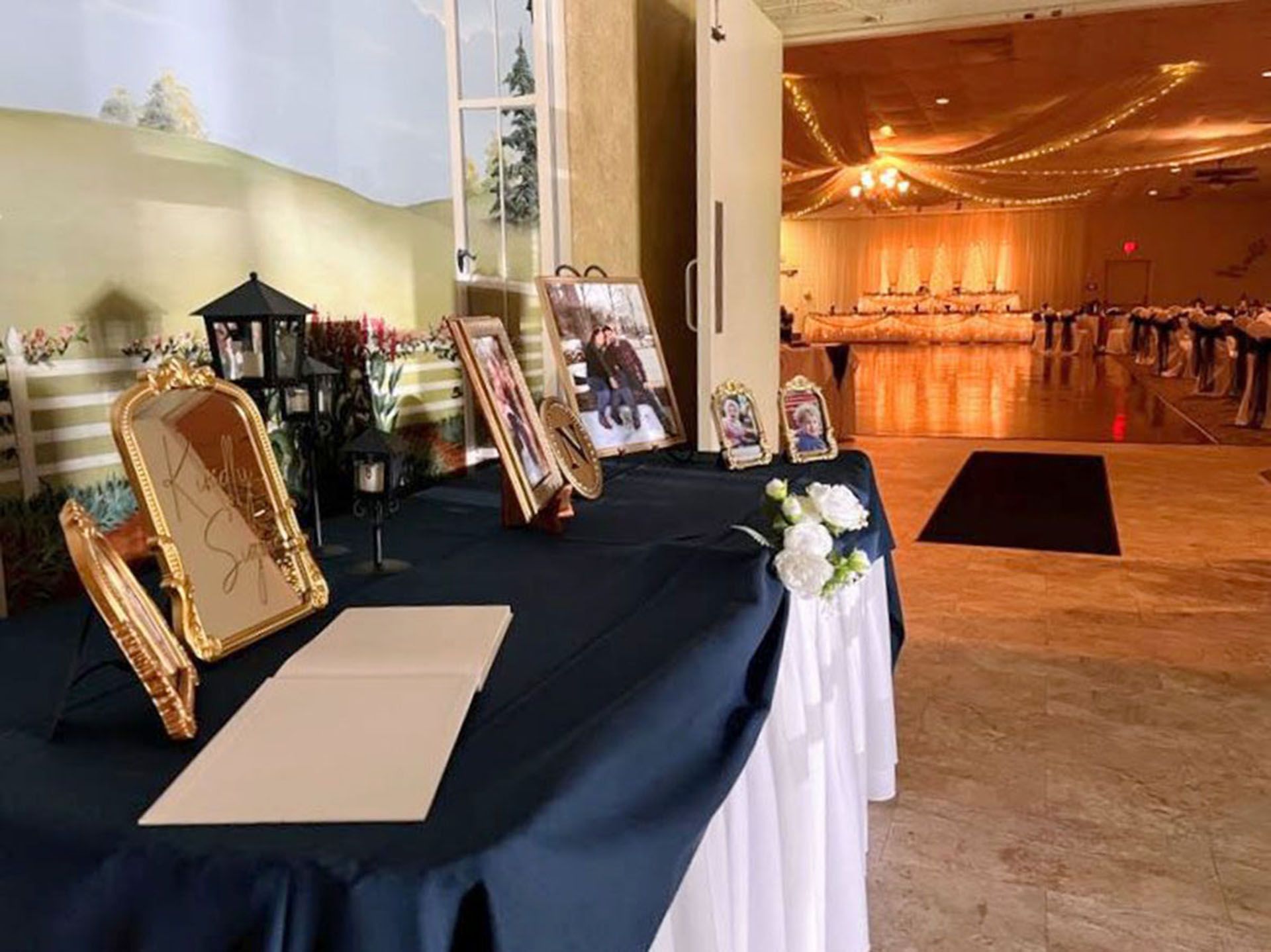 Table of framed photos and candles beside an event hall with warm orange lighting