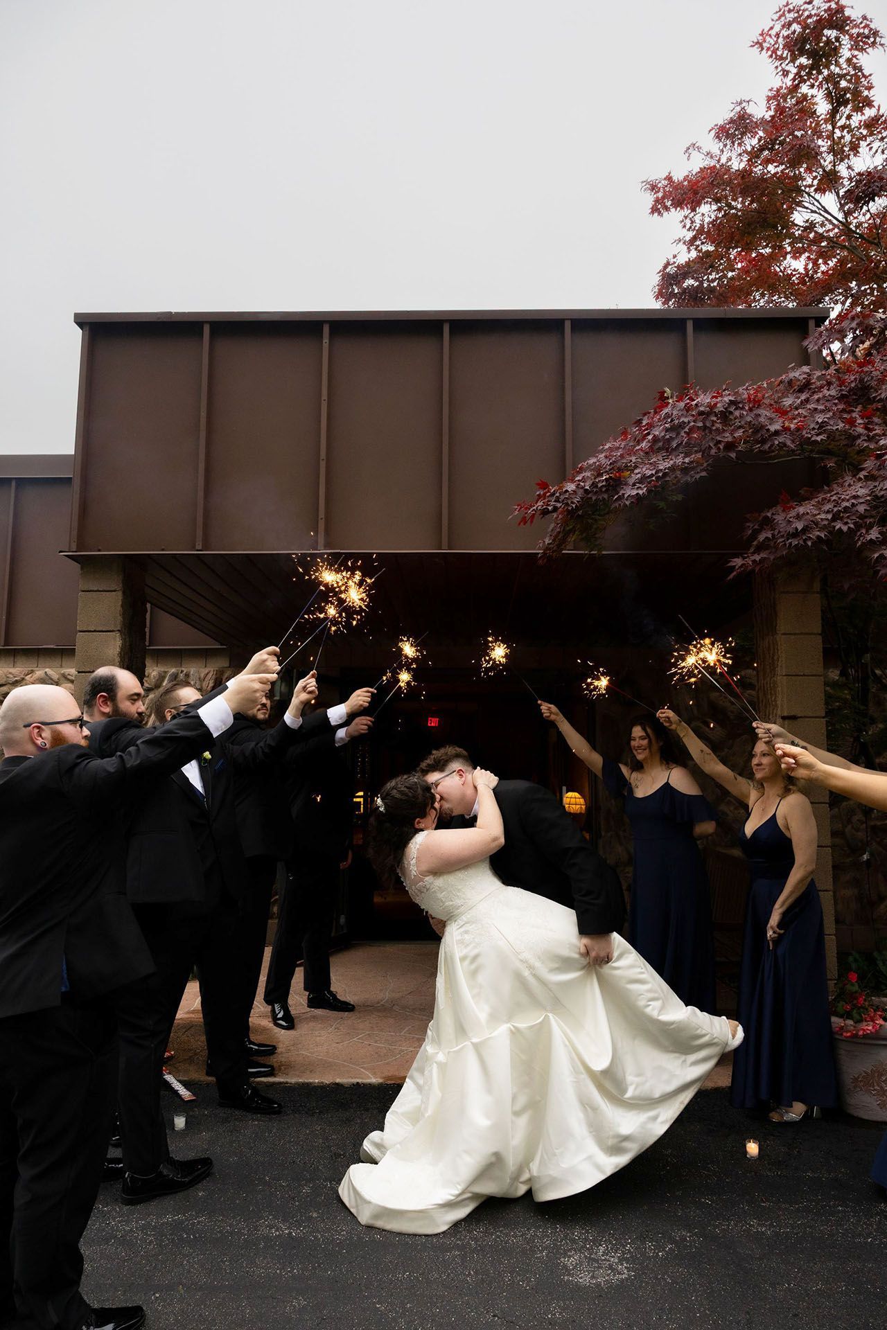 Bride and groom kiss as guests hold sparklers outside a venue