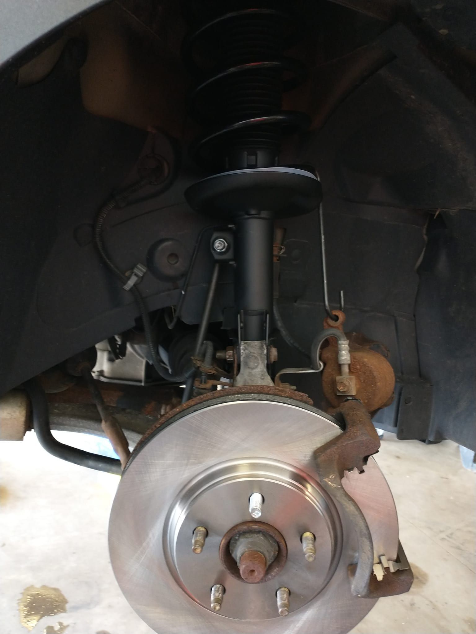 A close up of a car 's front suspension and brake disc.