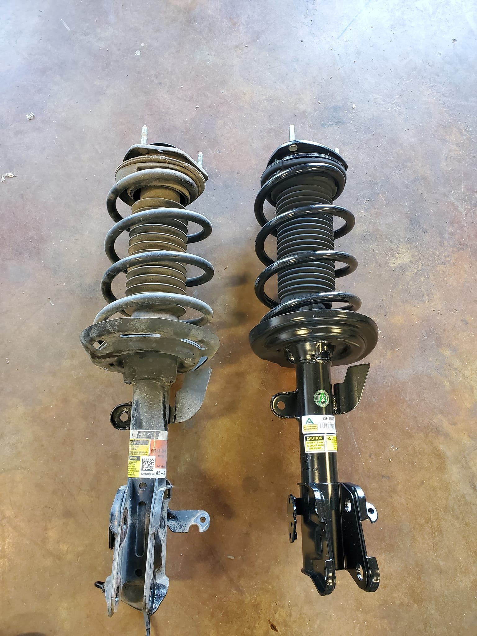 Two shock absorbers are sitting next to each other on a concrete floor.