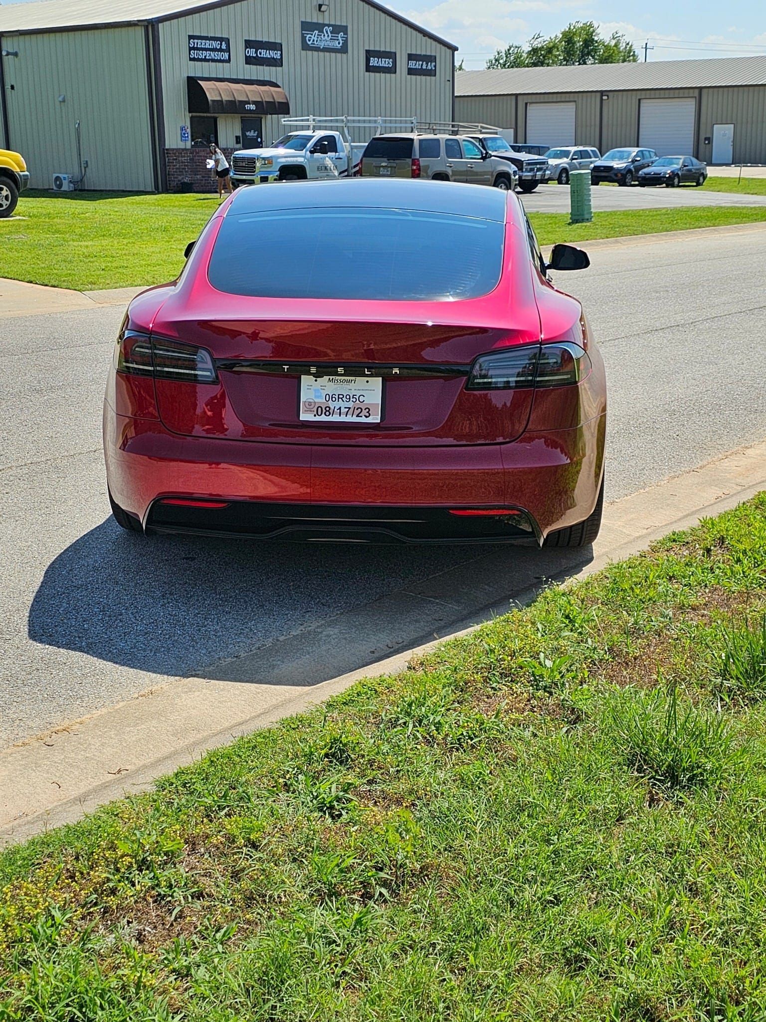 A red tesla model s is parked on the side of the road in front of a building.
