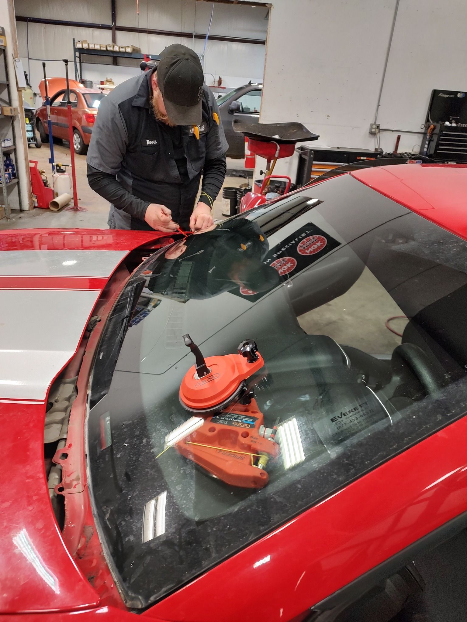 A man is fixing a windshield on a red car in a garage.