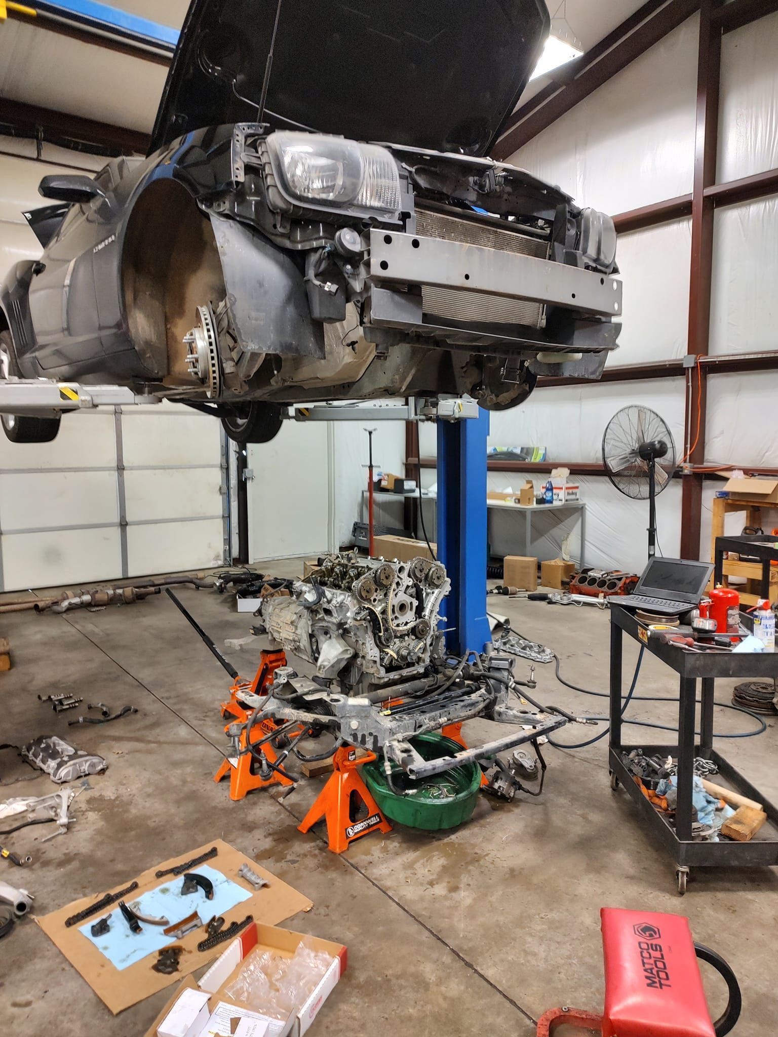 A car is being worked on in a garage with the hood up.