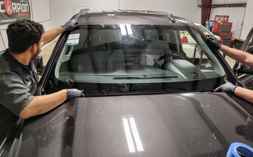 Two men are installing a windshield on a car.