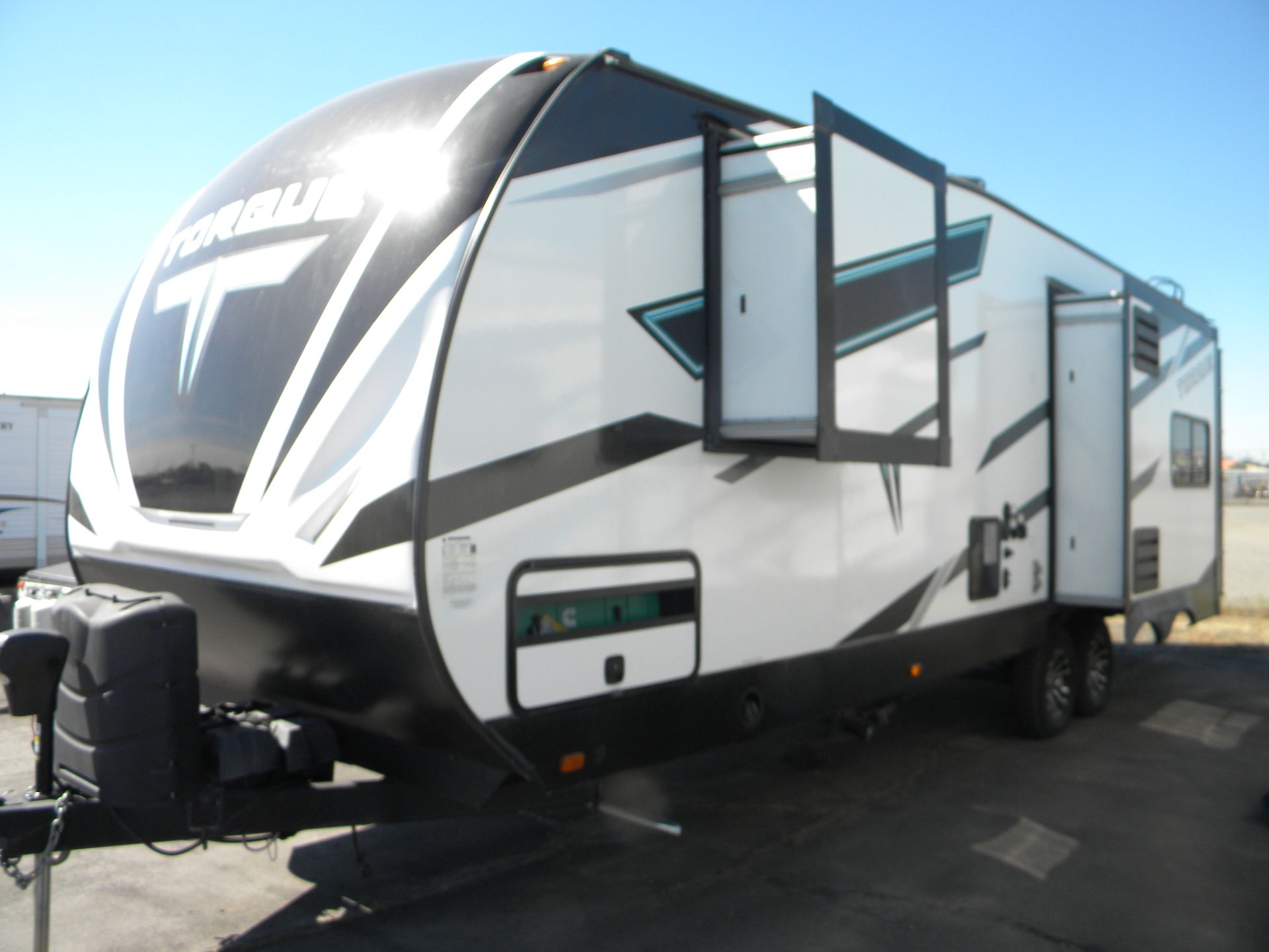 White travel trailer with black and gold geometric graphics, parked on a paved lot with two slide-outs extended.