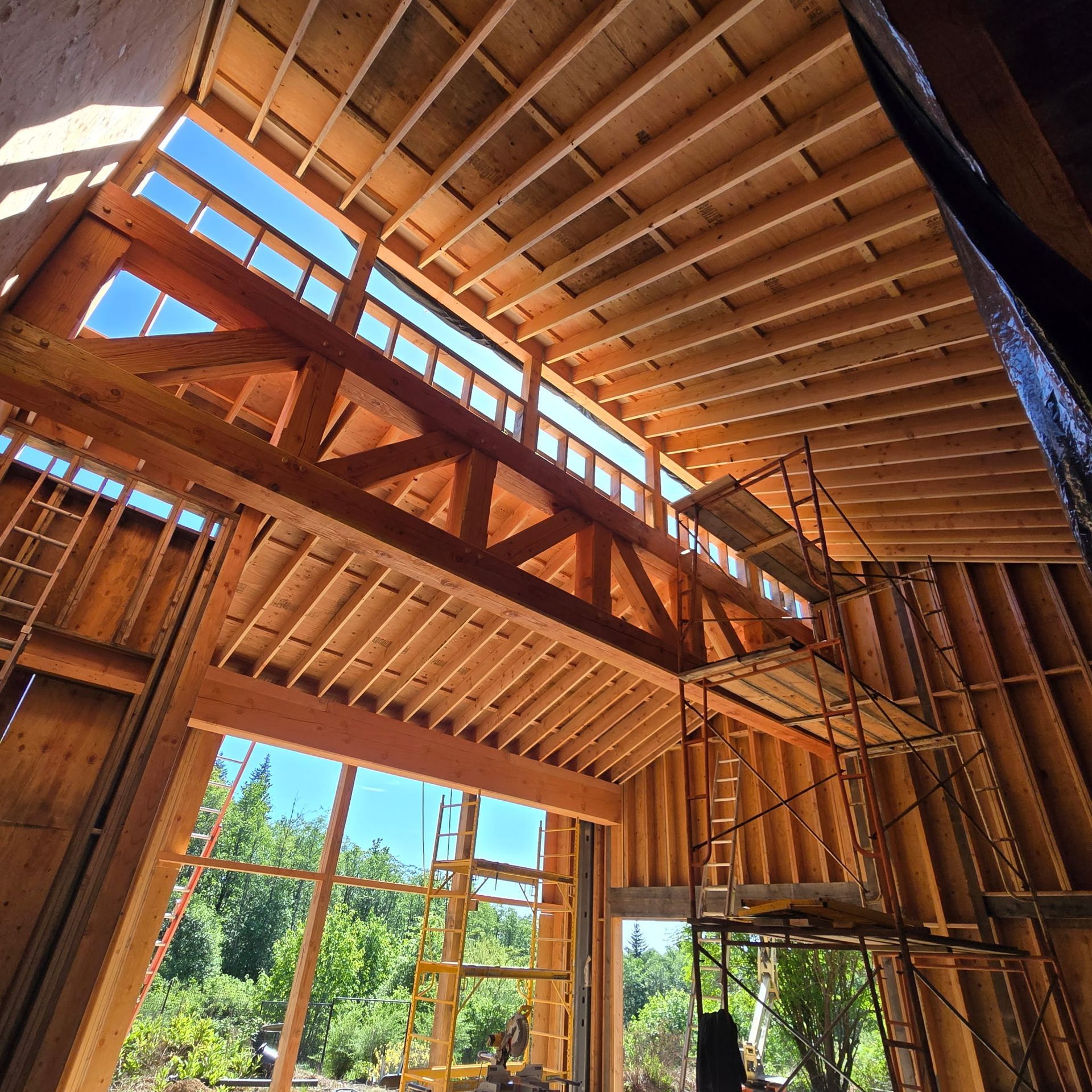 Interior of a timber-framed building under construction with exposed beams and large window openings.