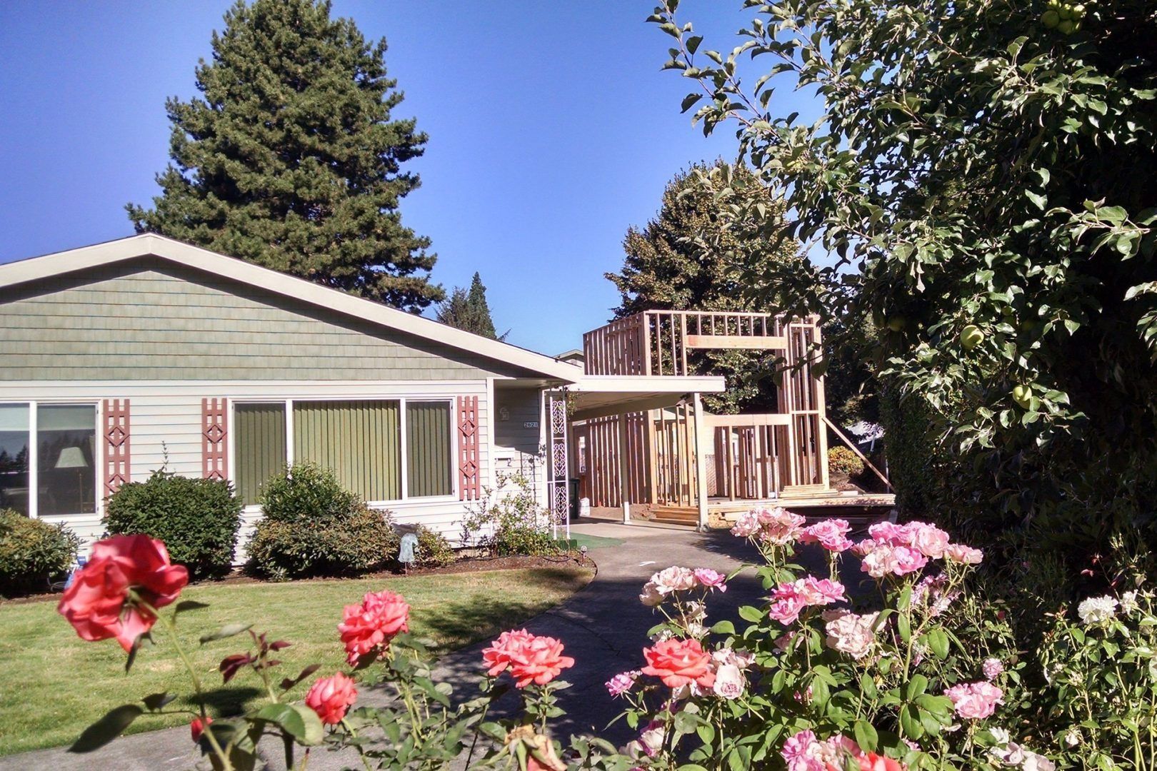 House exterior with construction; roses in foreground, trees and clear sky.