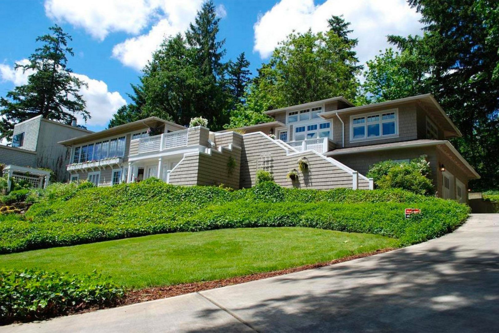 Modern house on a hillside with a green lawn, ivy, and a driveway, under a blue sky.