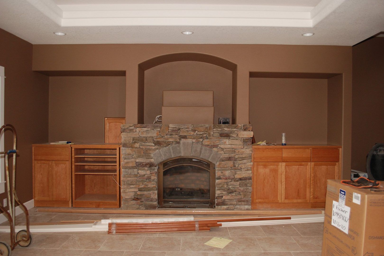 Stone fireplace with arched alcoves and unfinished wooden cabinetry in a room with brown walls.