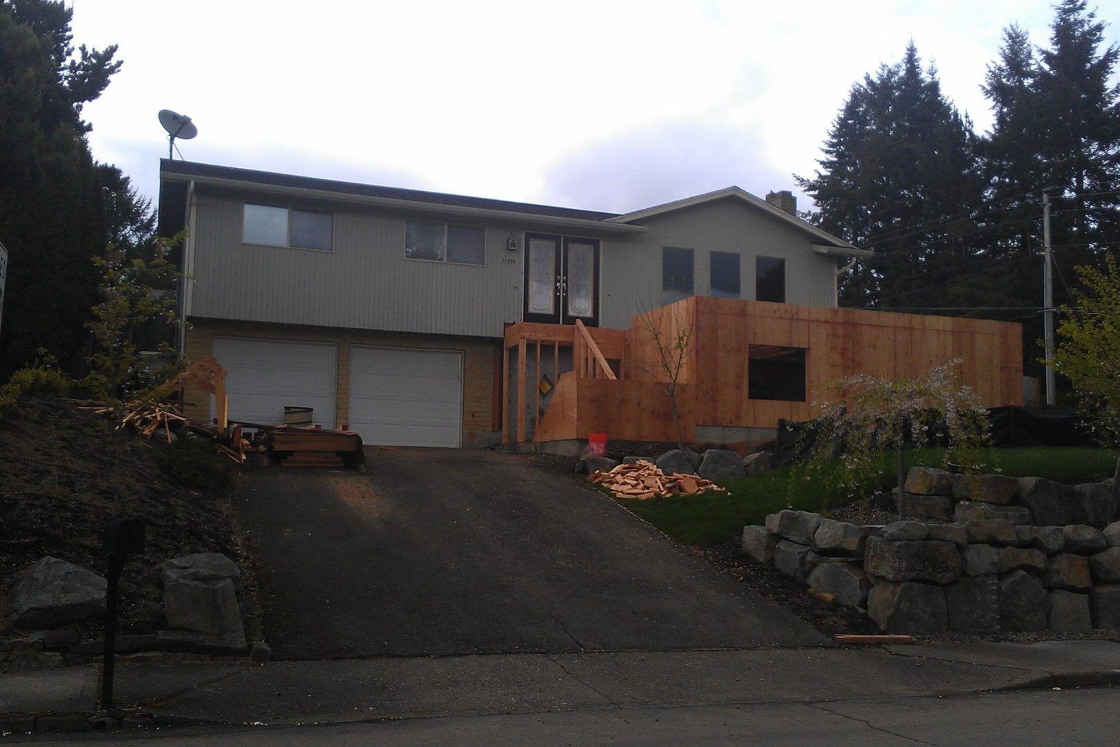 Two-story house undergoing construction. Exterior walls are wood. Driveway leads up to the garage.