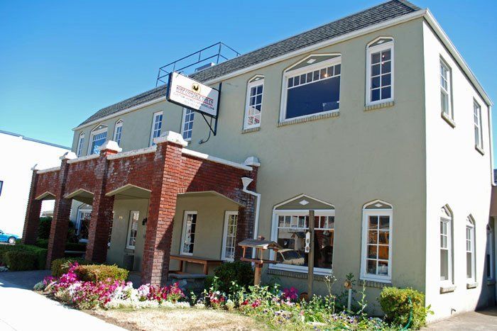 Two-story building with a red brick entrance and light green exterior. Sign above, flowers in front.