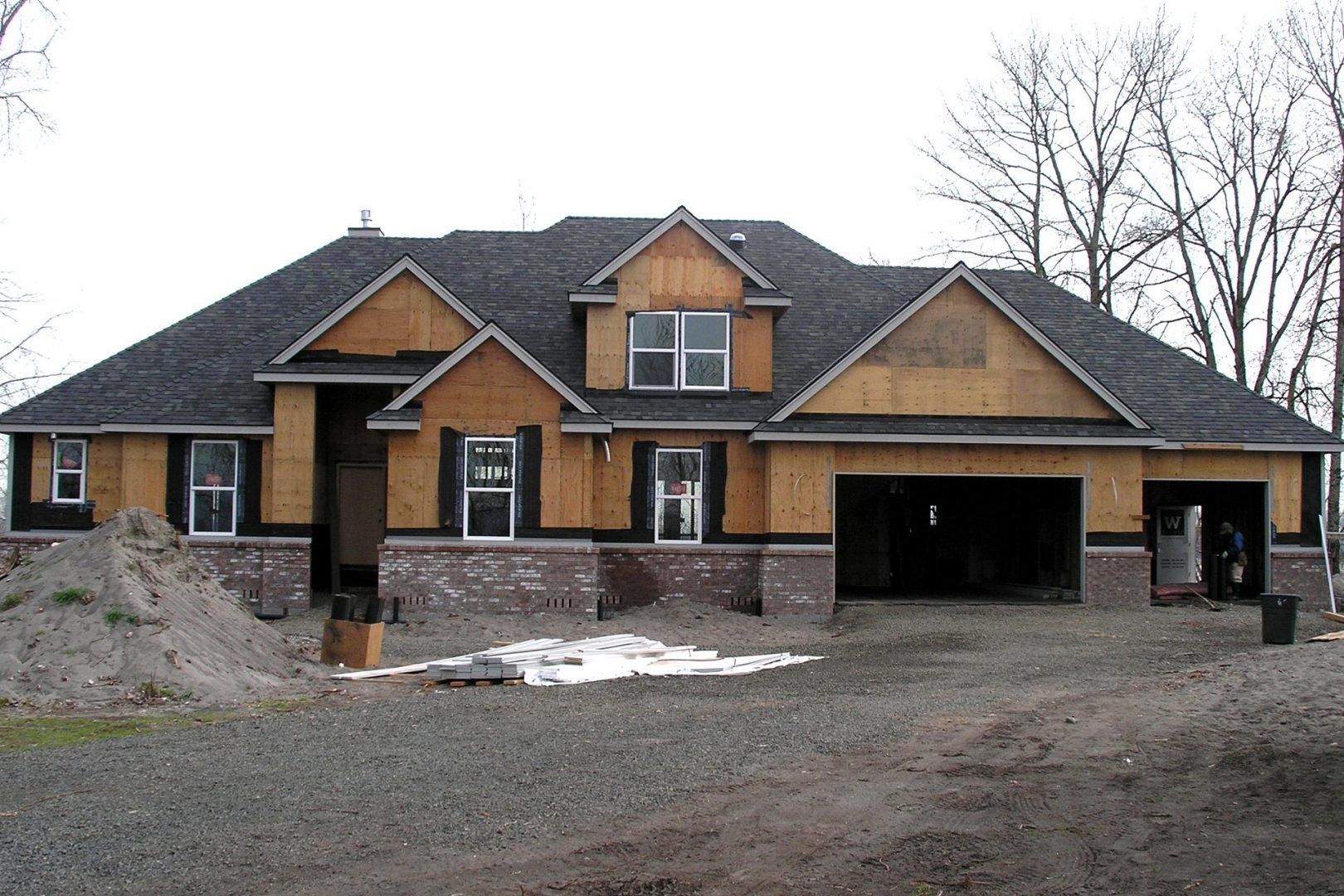 House under construction with exposed wood frame, brick foundation, and garage.