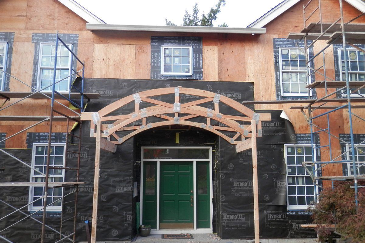 House exterior under construction, with wooden archway over a green door, surrounded by scaffolding.