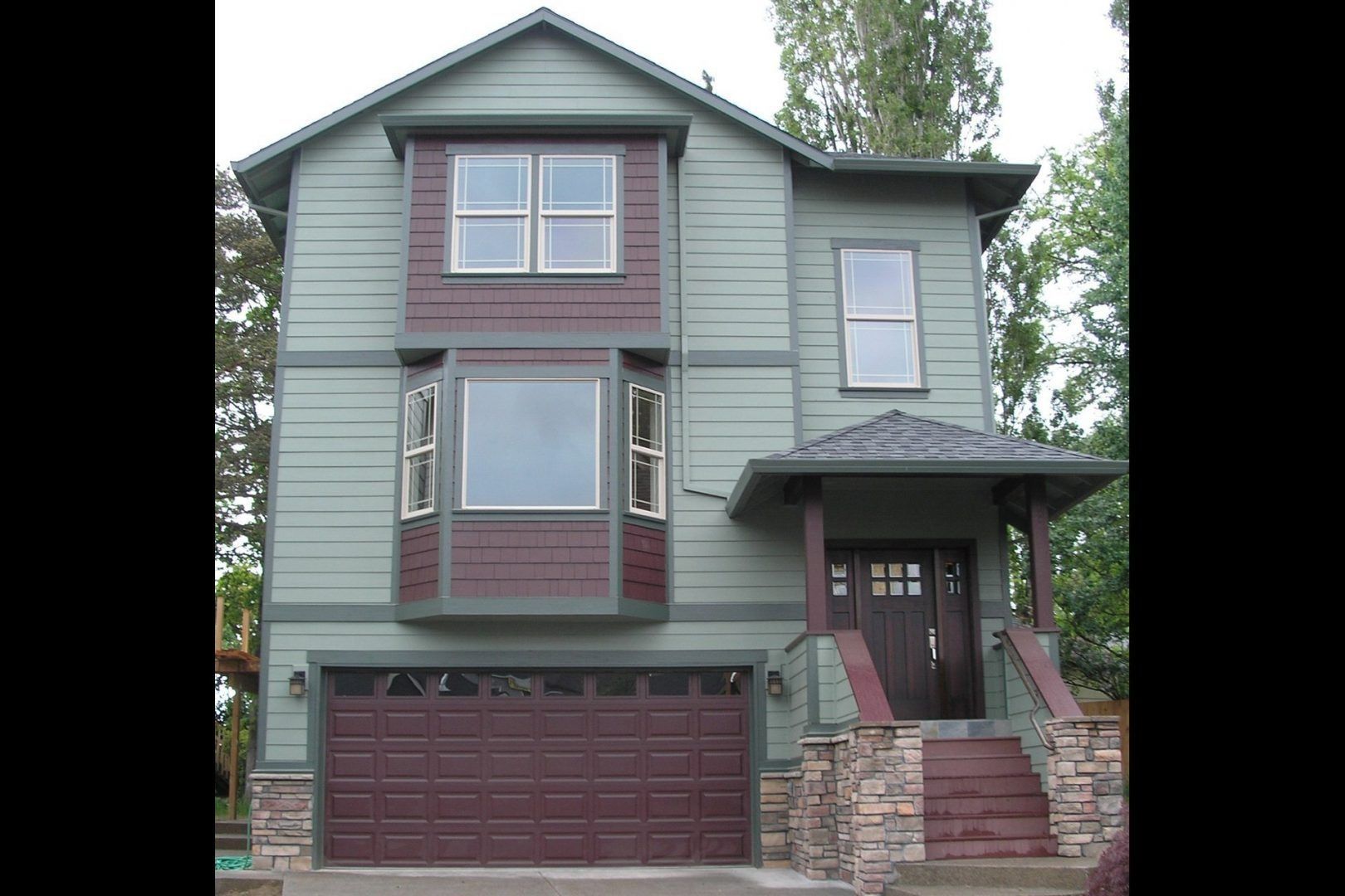 Two-story house with green siding, brown trim, and a brown garage door. Entrance with porch and stairs.