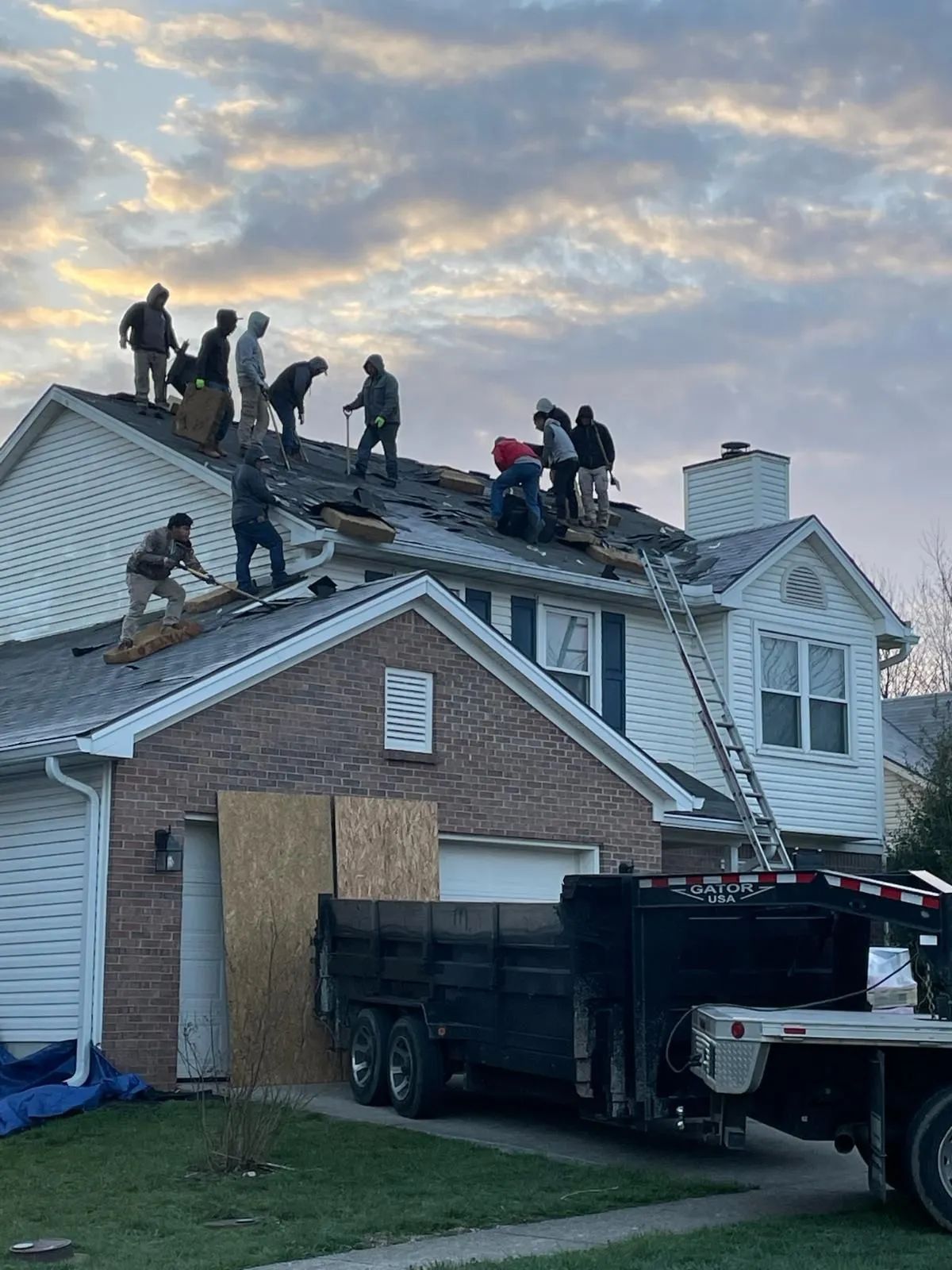 Roofers replacing shingles on a house. Workers on roof, truck with tools in front, cloudy sky.