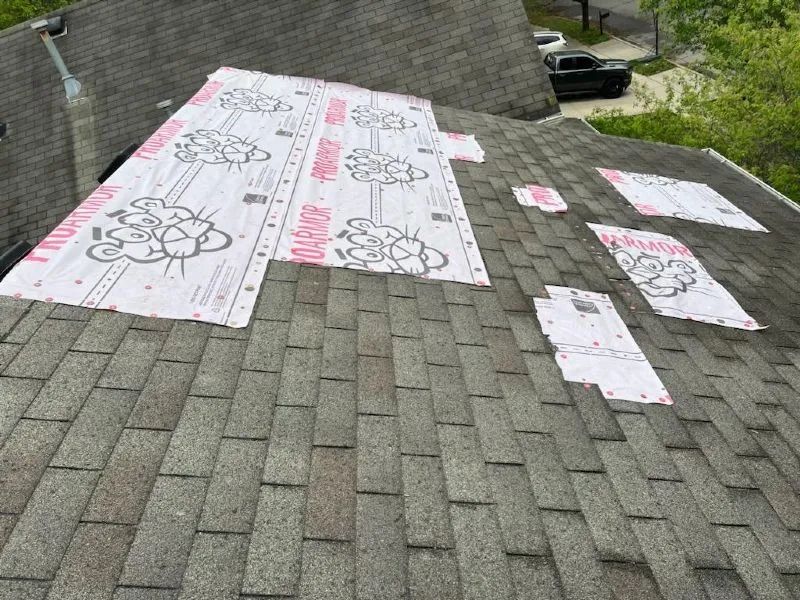 Roof with missing shingles and patches of pink underlayment material.