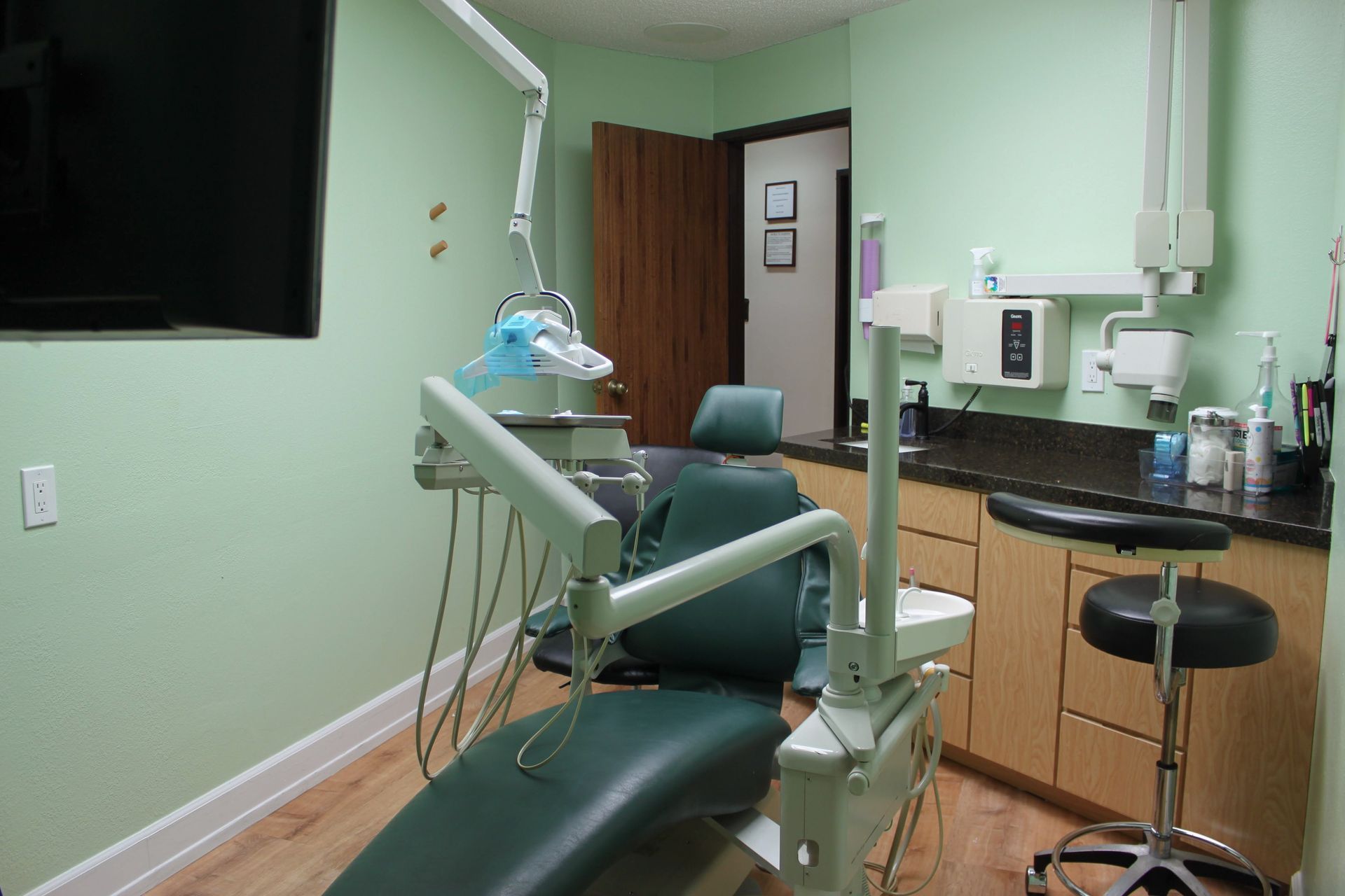 A dental office with a green chair and a black stool