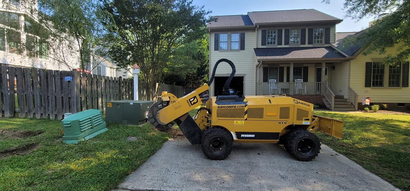 A yellow stump grinder on a driveway in front of a house.