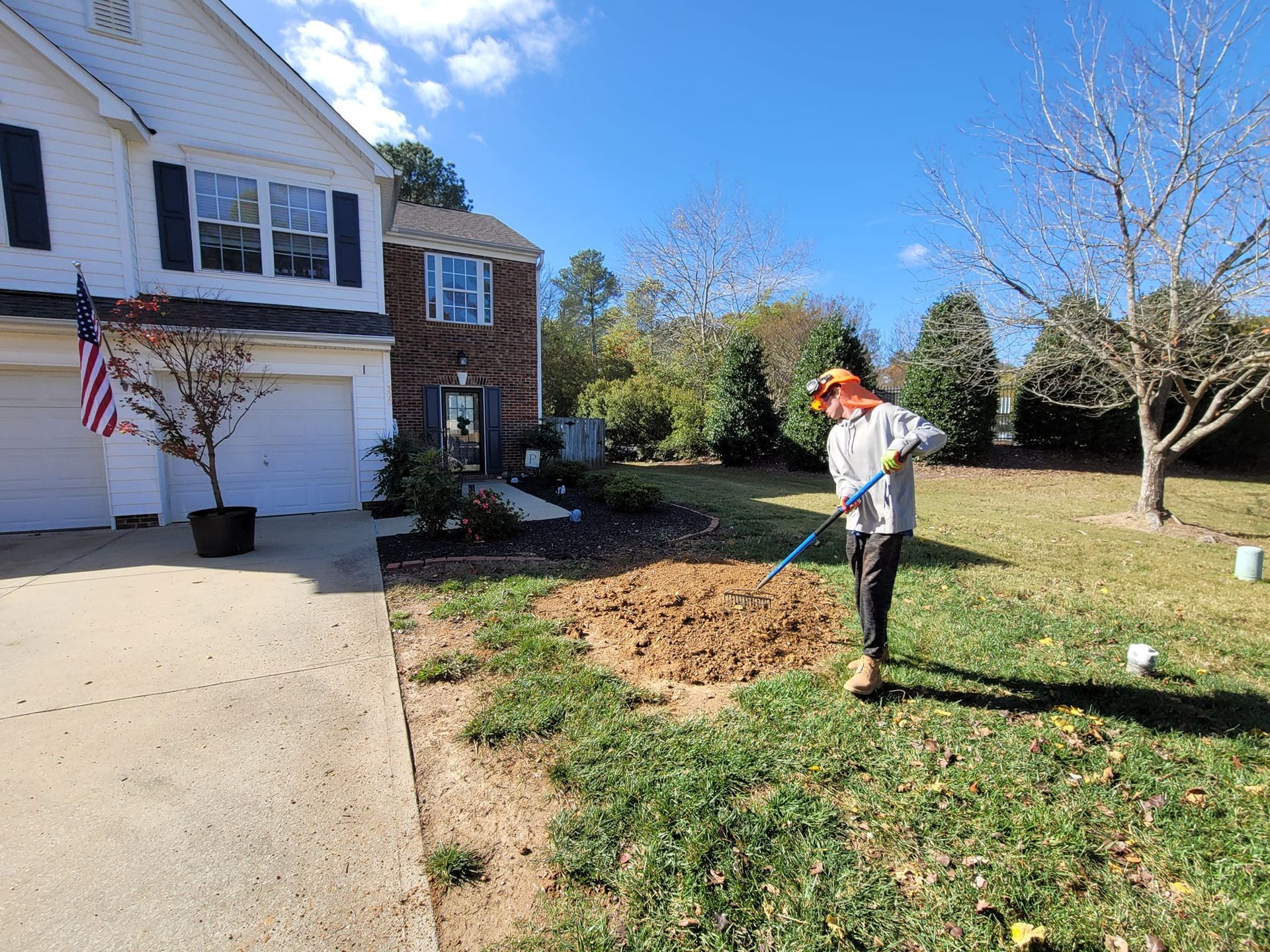 Person raking dirt in a yard near a house on a sunny day.