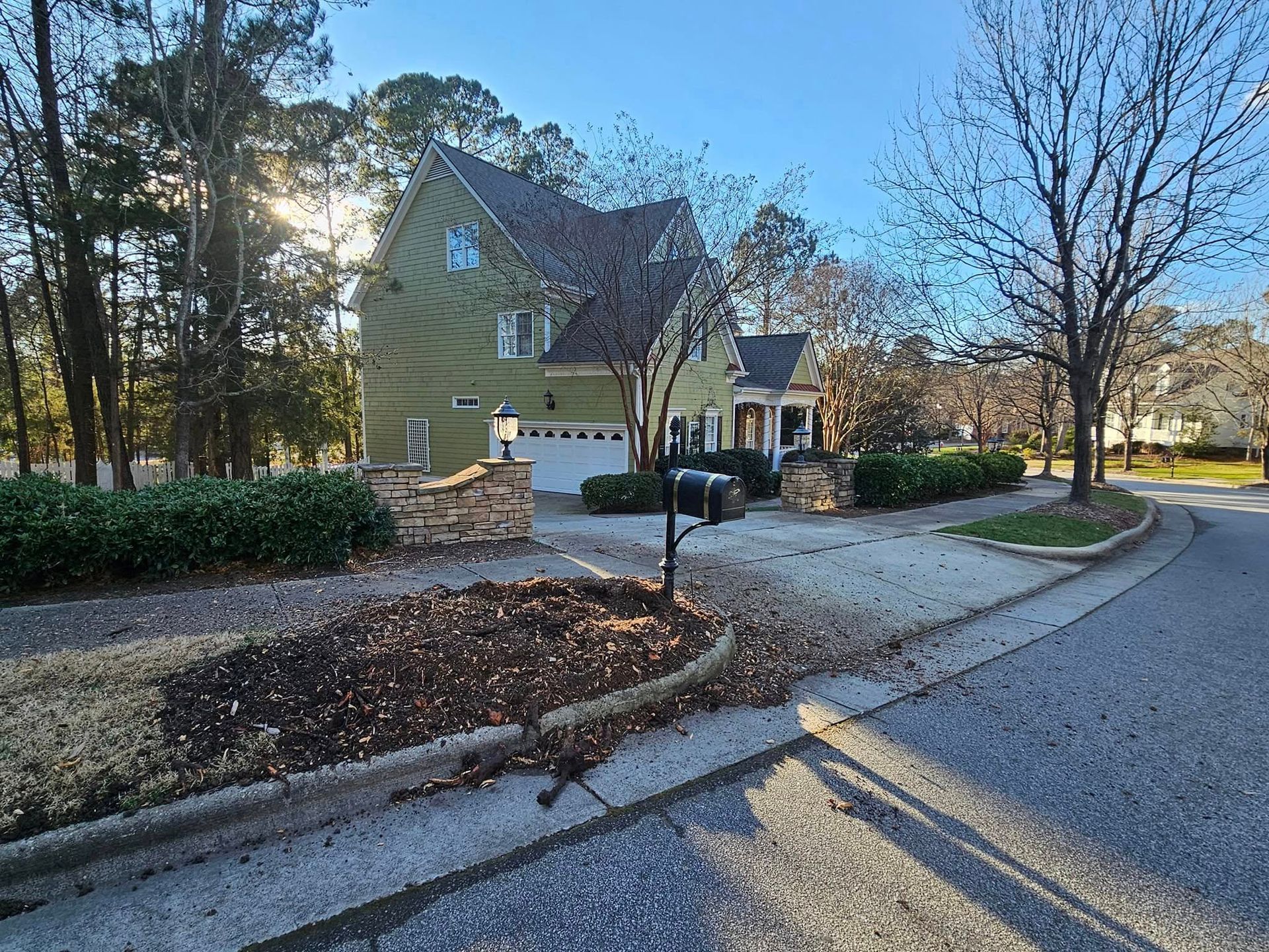 Green house with stone pillars, mailbox on a sunny day.