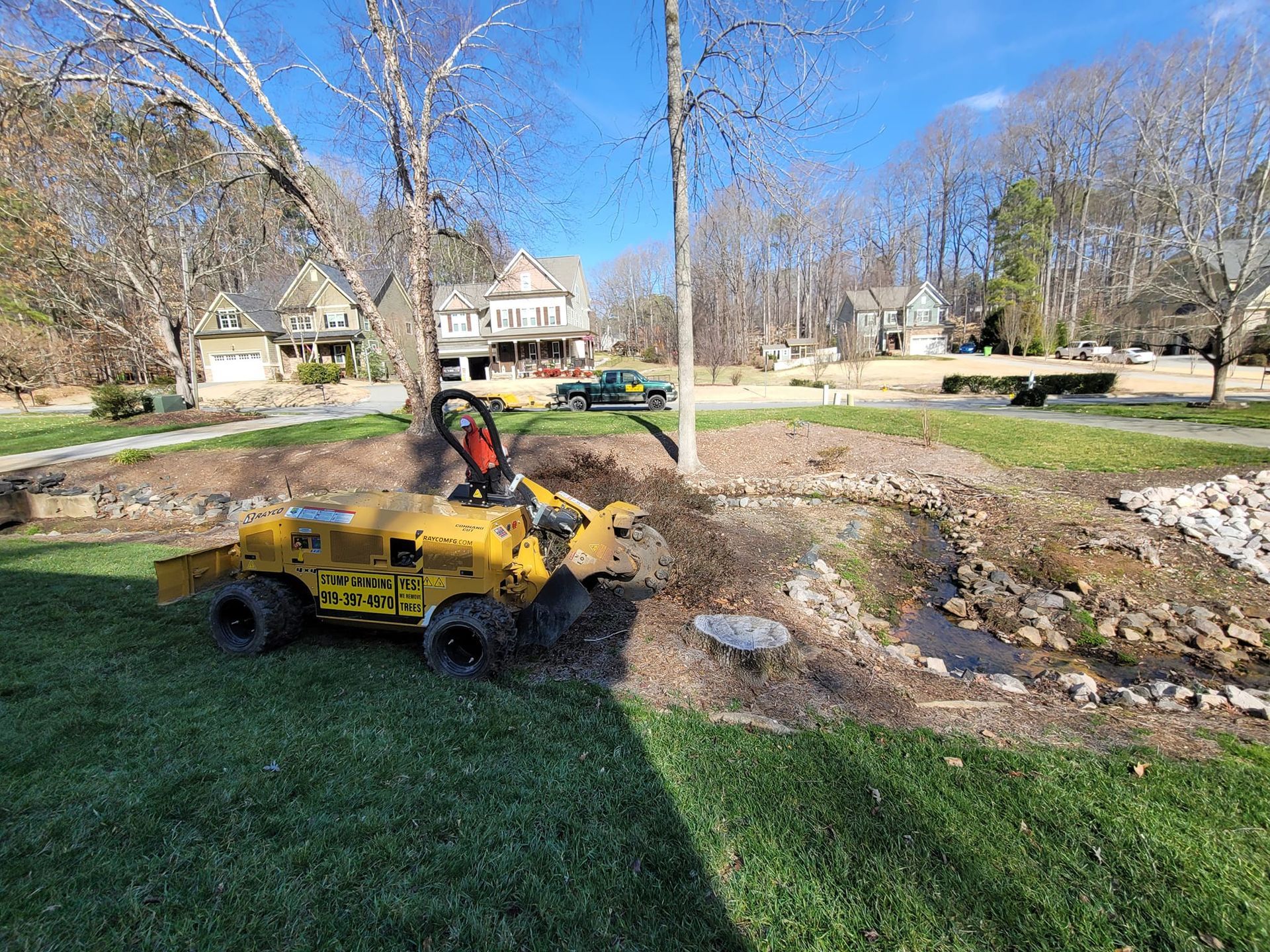 Yellow stump grinder removing a tree stump next to a small stream in a residential yard.