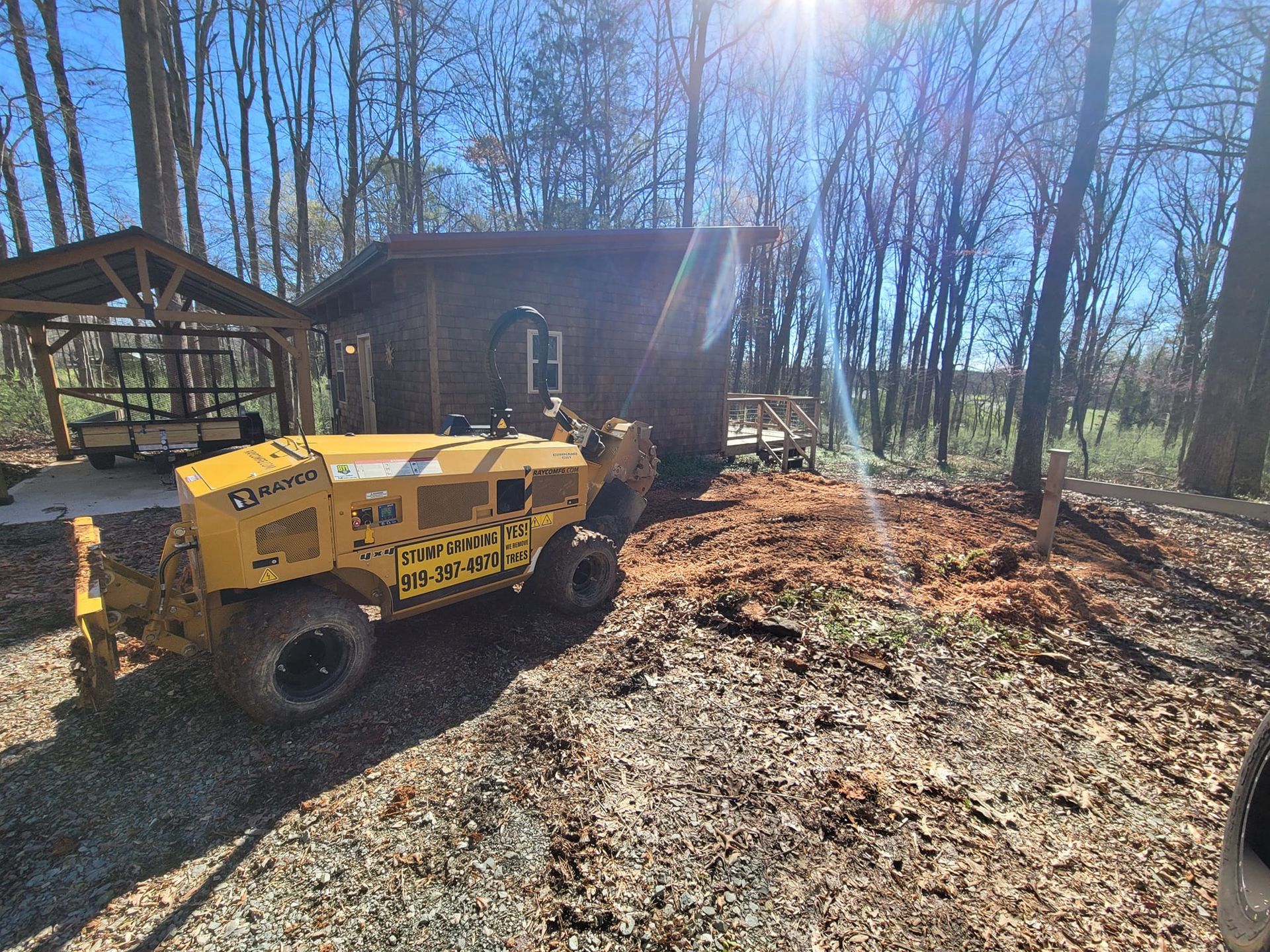 Yellow tracked vehicle near a small cabin in a wooded area on a sunny day.