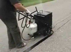 Man using asphalt sealer equipment on driveway