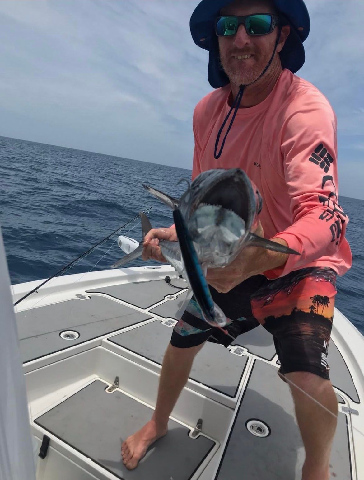 A man in a pink shirt is holding a fish on a boat
