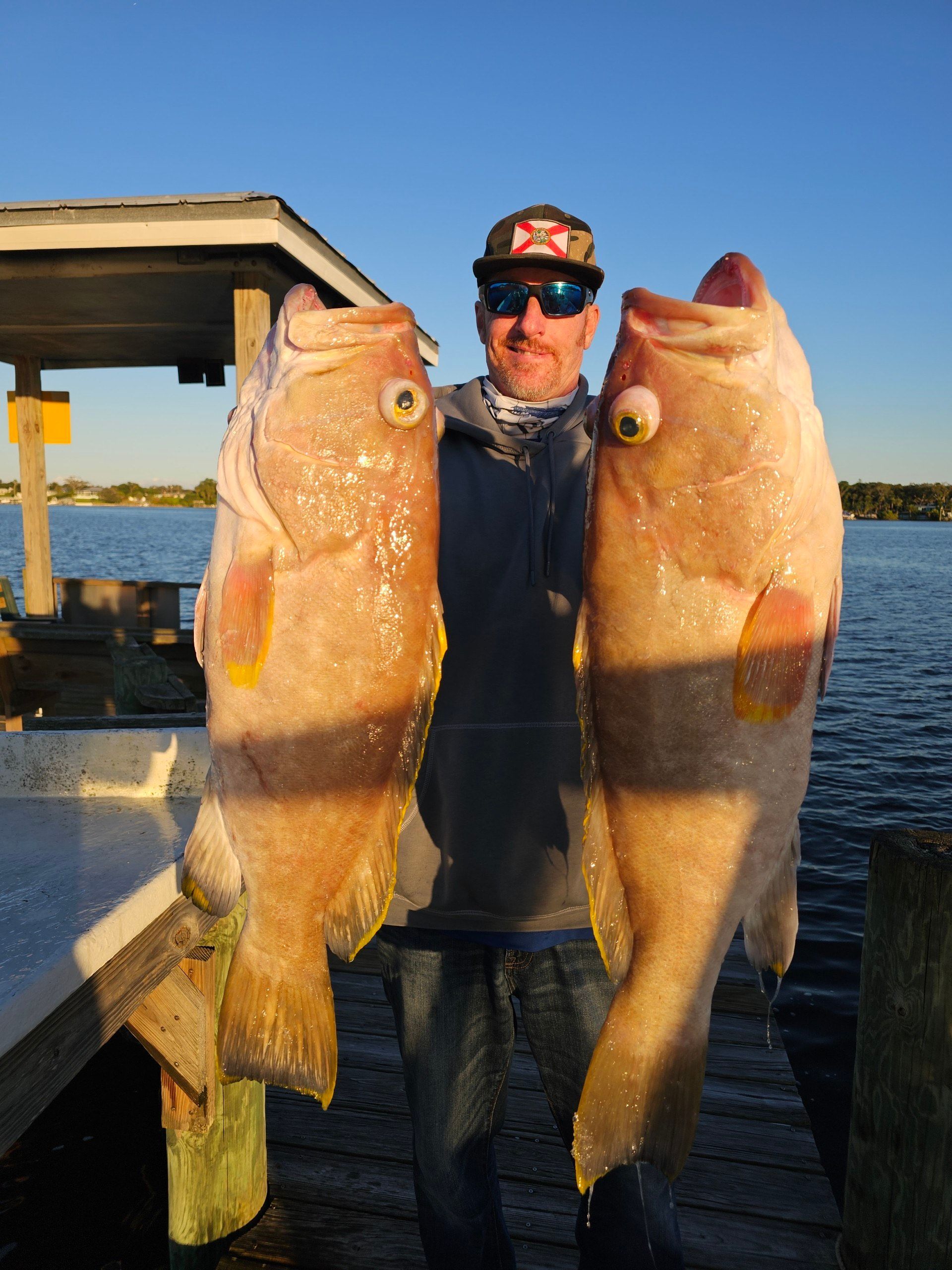 A man is holding two large fish on a dock
